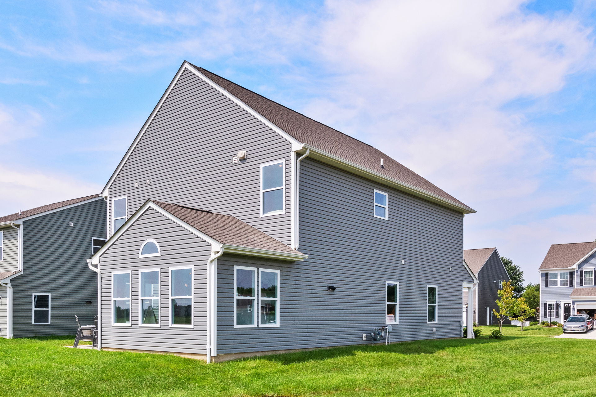 Modern gray two-story house with large windows and a well-maintained lawn under a clear blue sky.