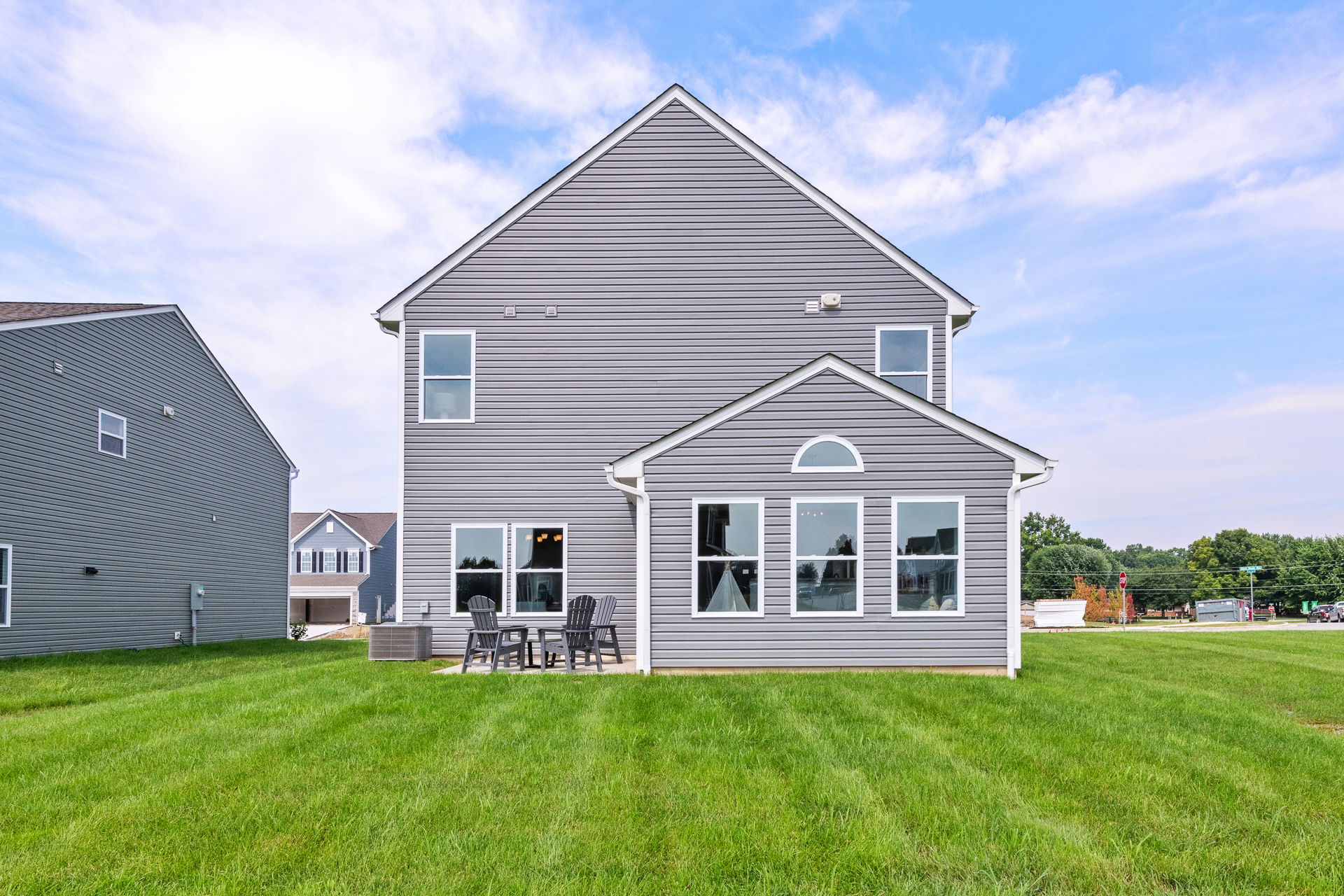 Modern gray two-story house with large backyard and patio furniture set.