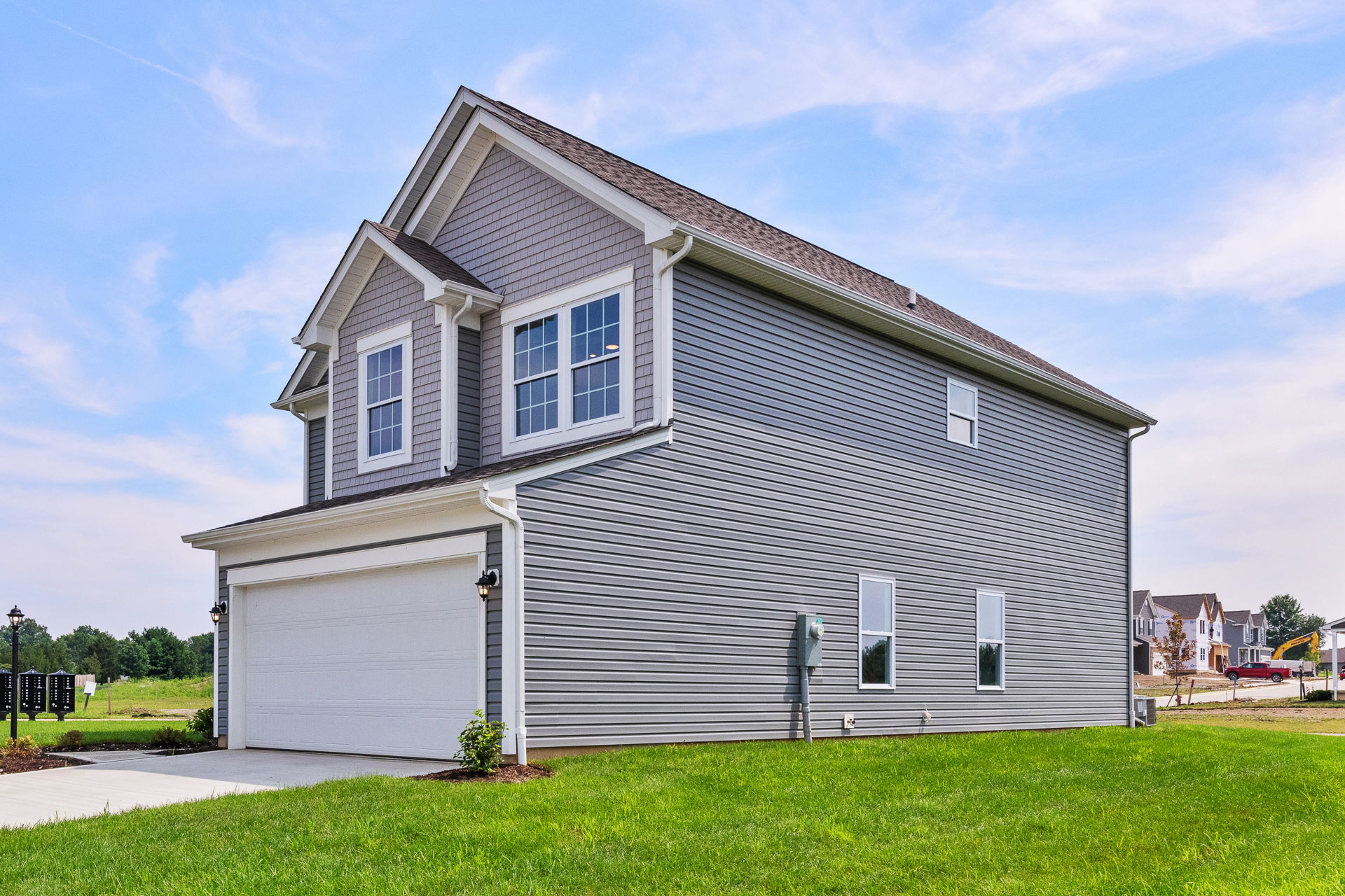 Modern two-story gray house with a white garage, set against a clear blue sky and green lawn.