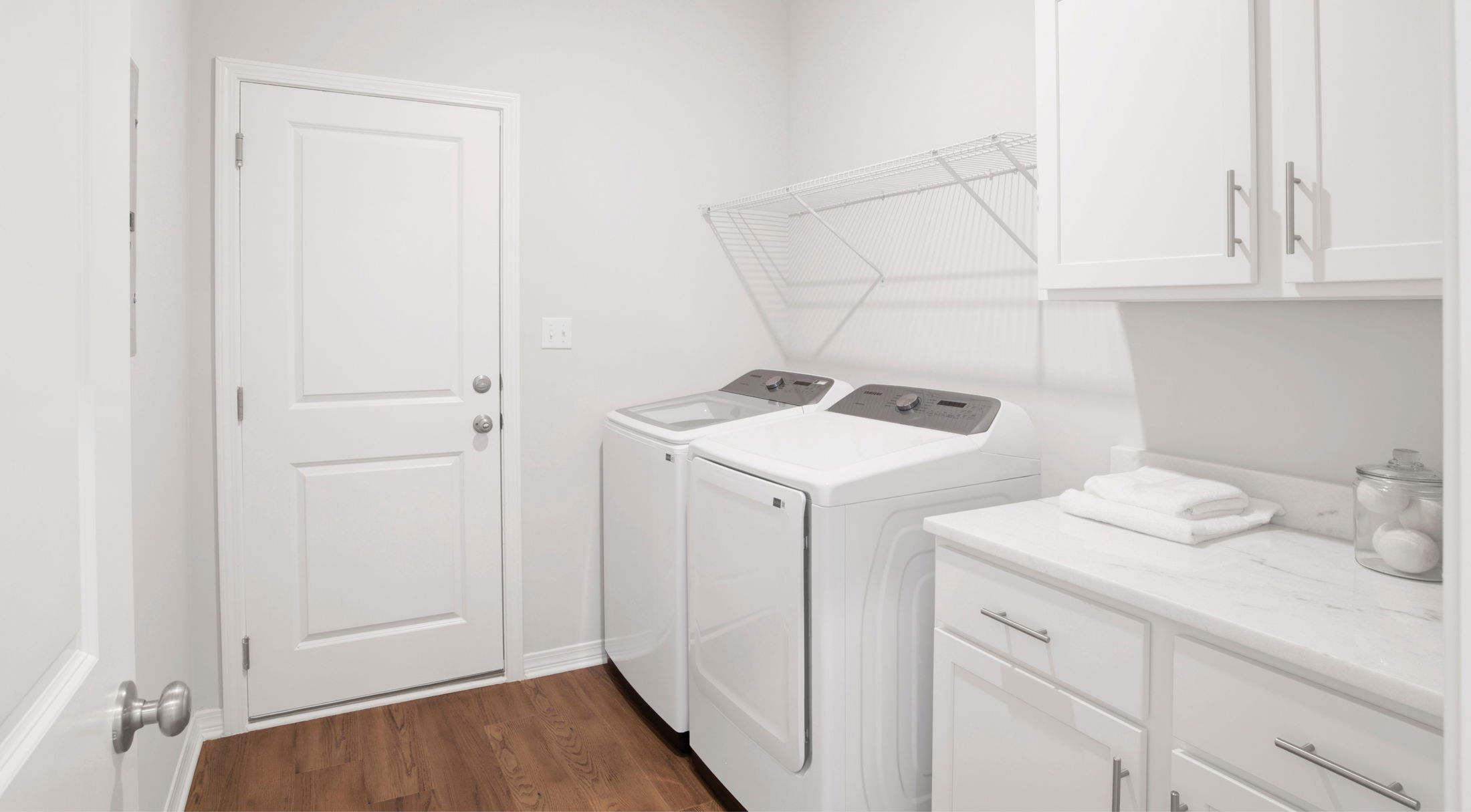 Modern laundry room with white washer and dryer, wood flooring, and white cabinetry.
