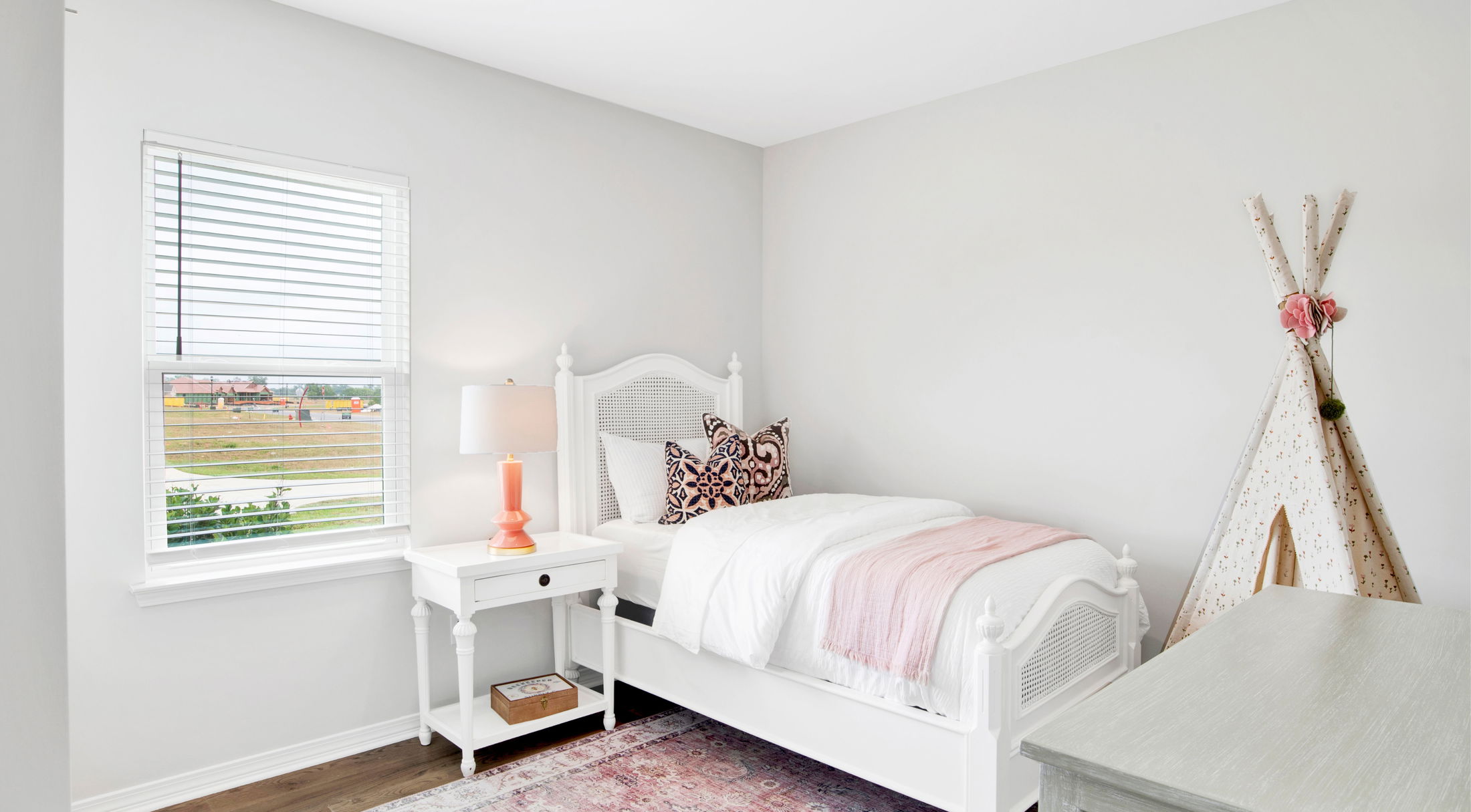 Bright and airy children's bedroom with a white bed, patterned pillows, teepee tent, and natural light from a window.