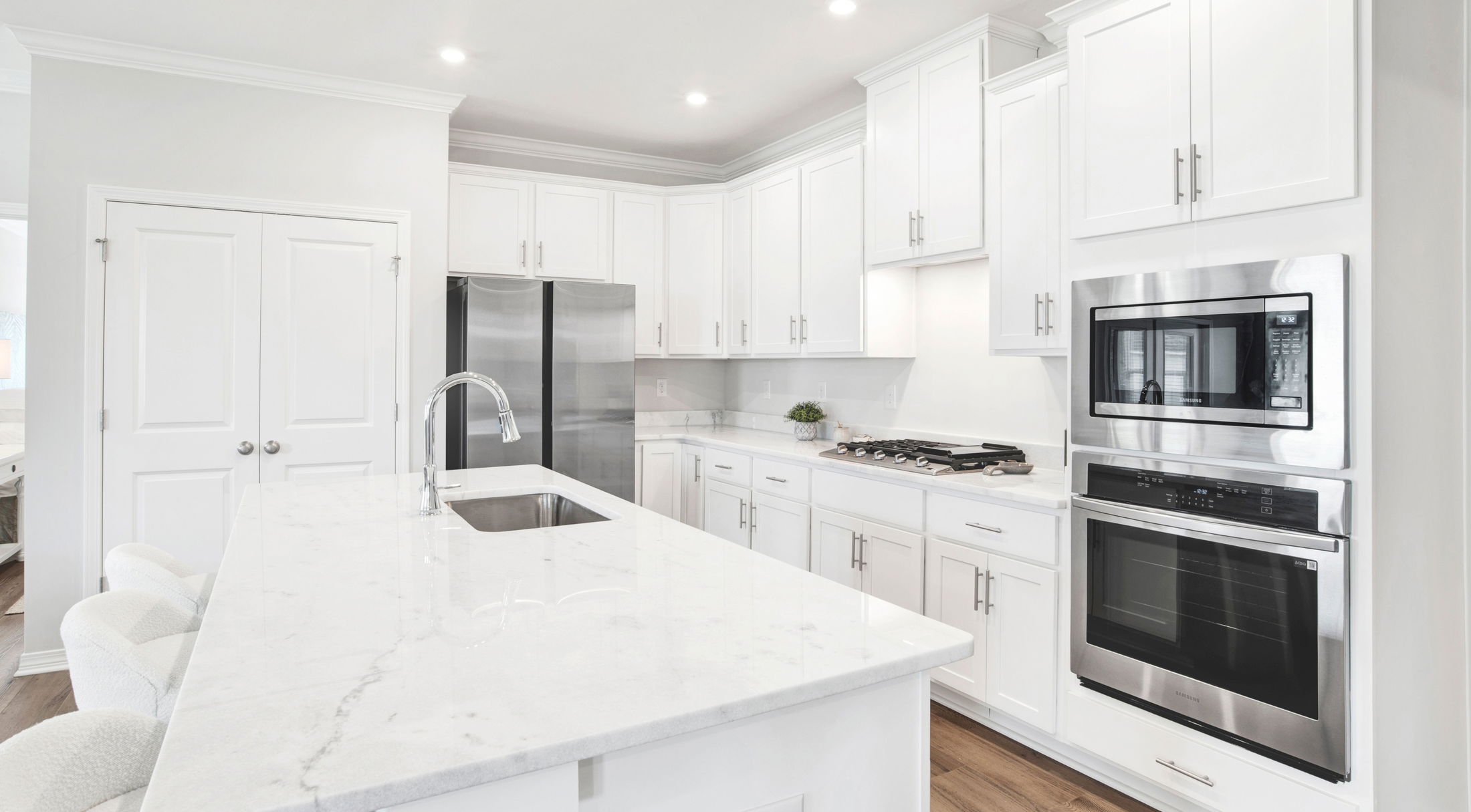 Modern white kitchen with marble countertops, stainless steel appliances, and sleek cabinetry.