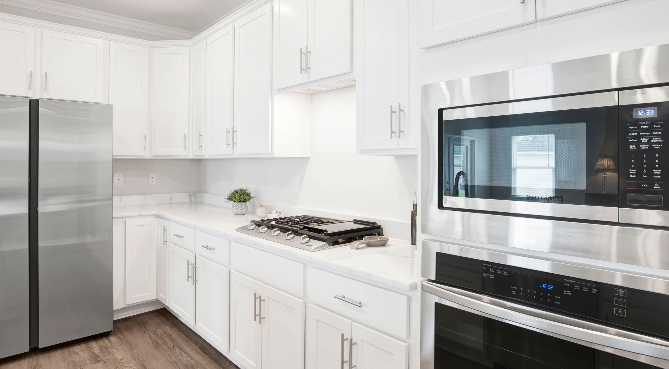 Modern kitchen with stainless steel appliances, white cabinets, and a gas stove on a marble countertop.