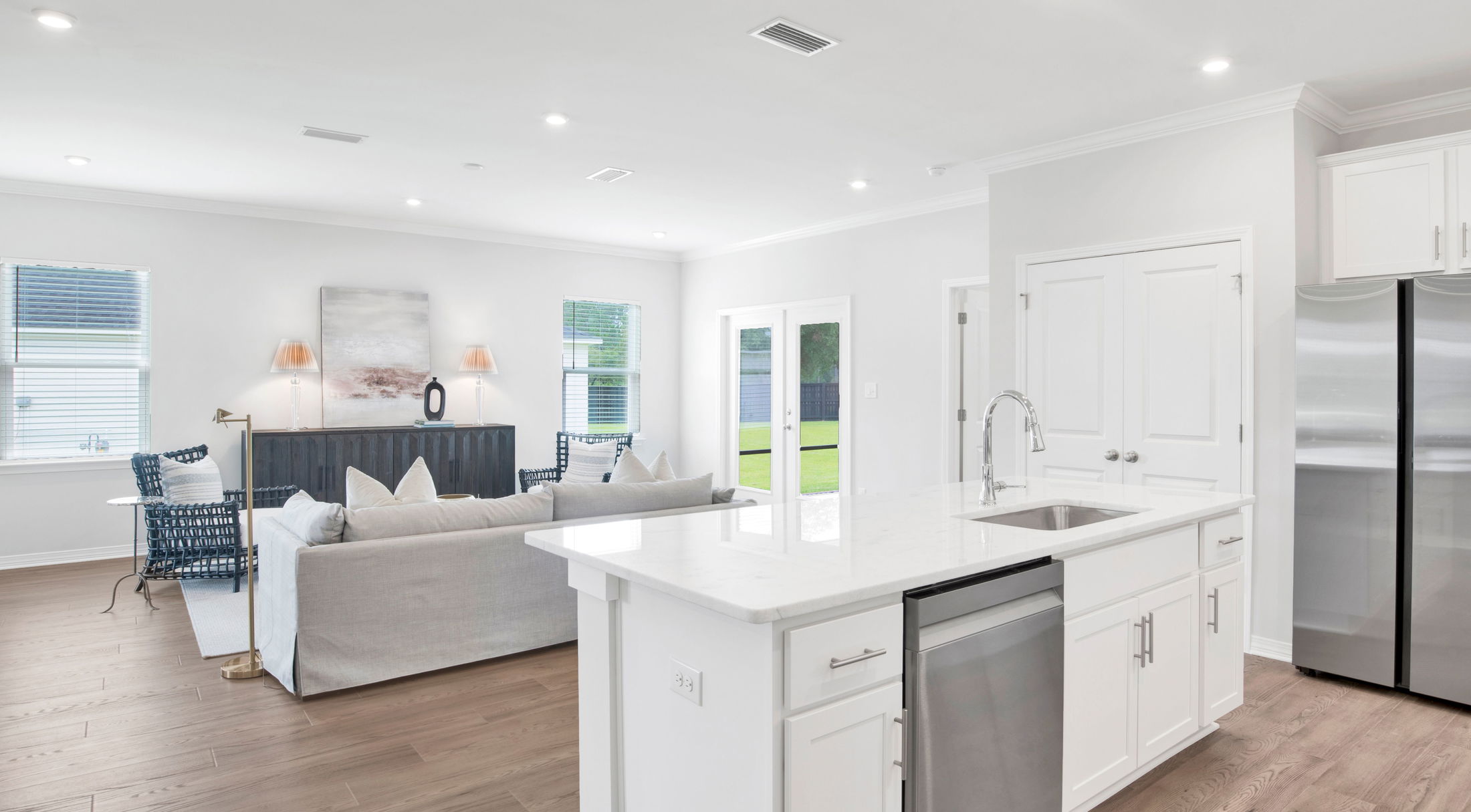 Modern open-concept living room and kitchen with white cabinetry, stainless steel appliances, and a sleek island countertop.