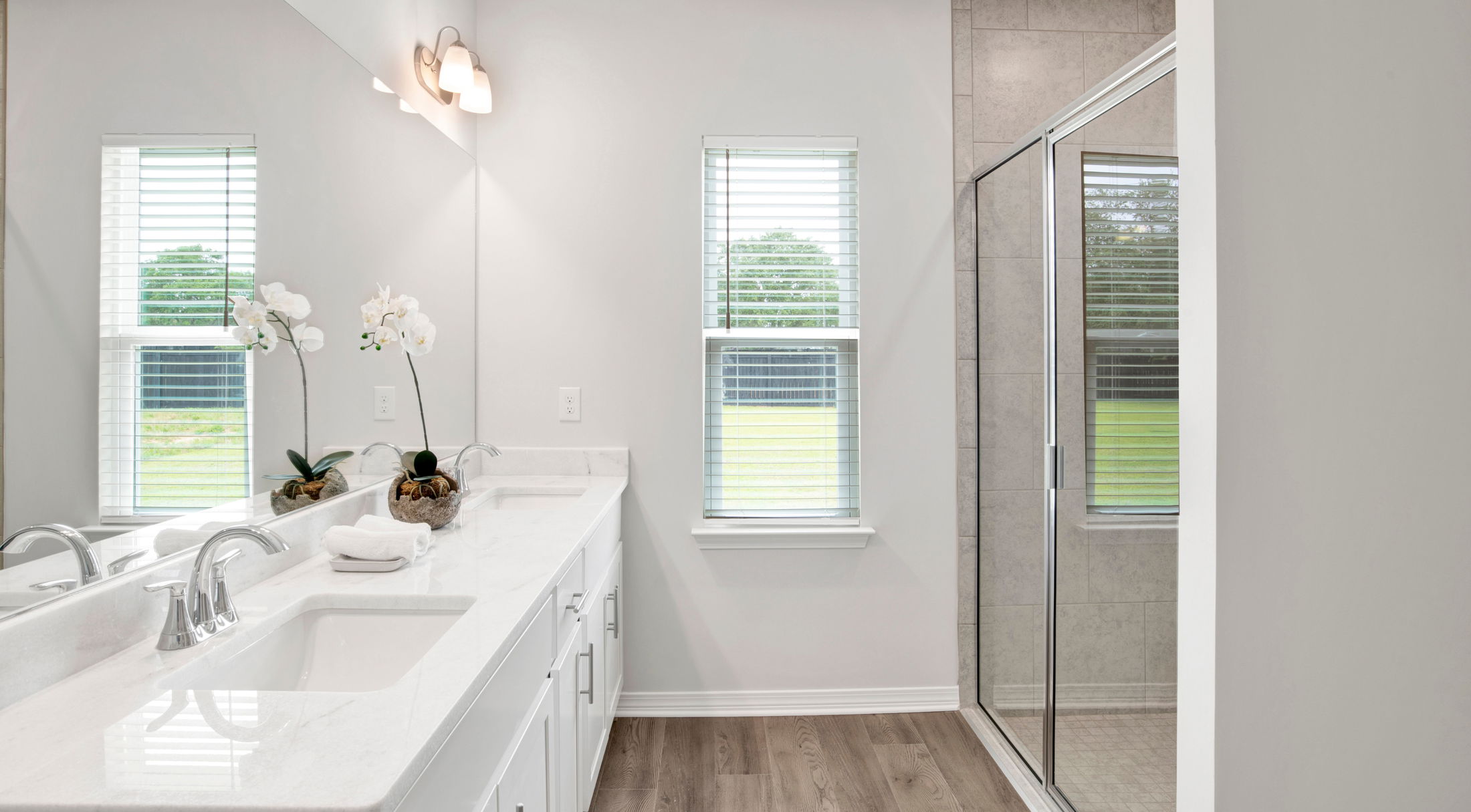 Modern bathroom with double sink vanity, white countertops, and glass shower enclosure.