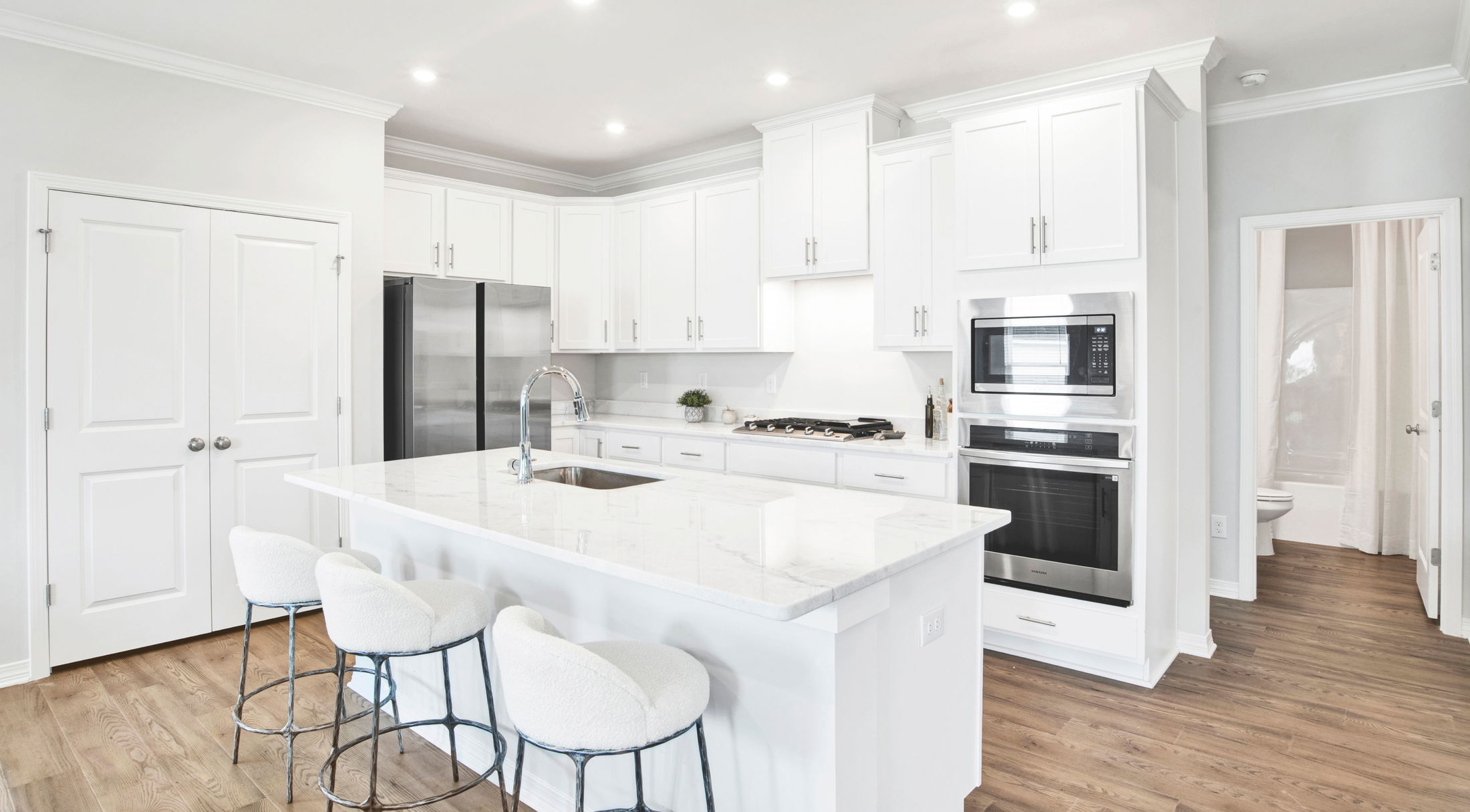 Modern white kitchen with sleek cabinetry, stainless steel appliances, and a marble island with bar stools.