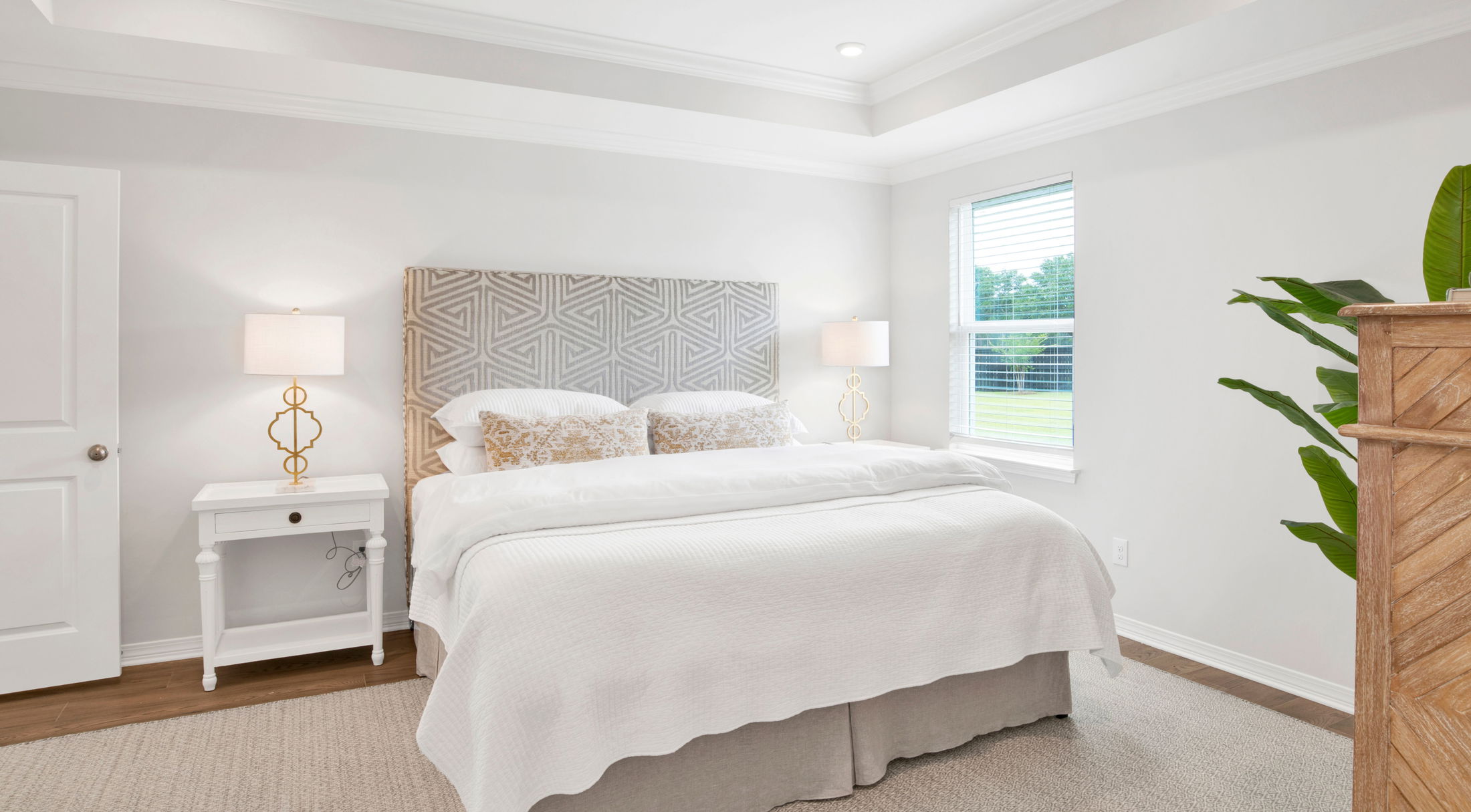 Spacious bedroom with large bed, patterned headboard, stylish bedside lamps, and natural light from window.