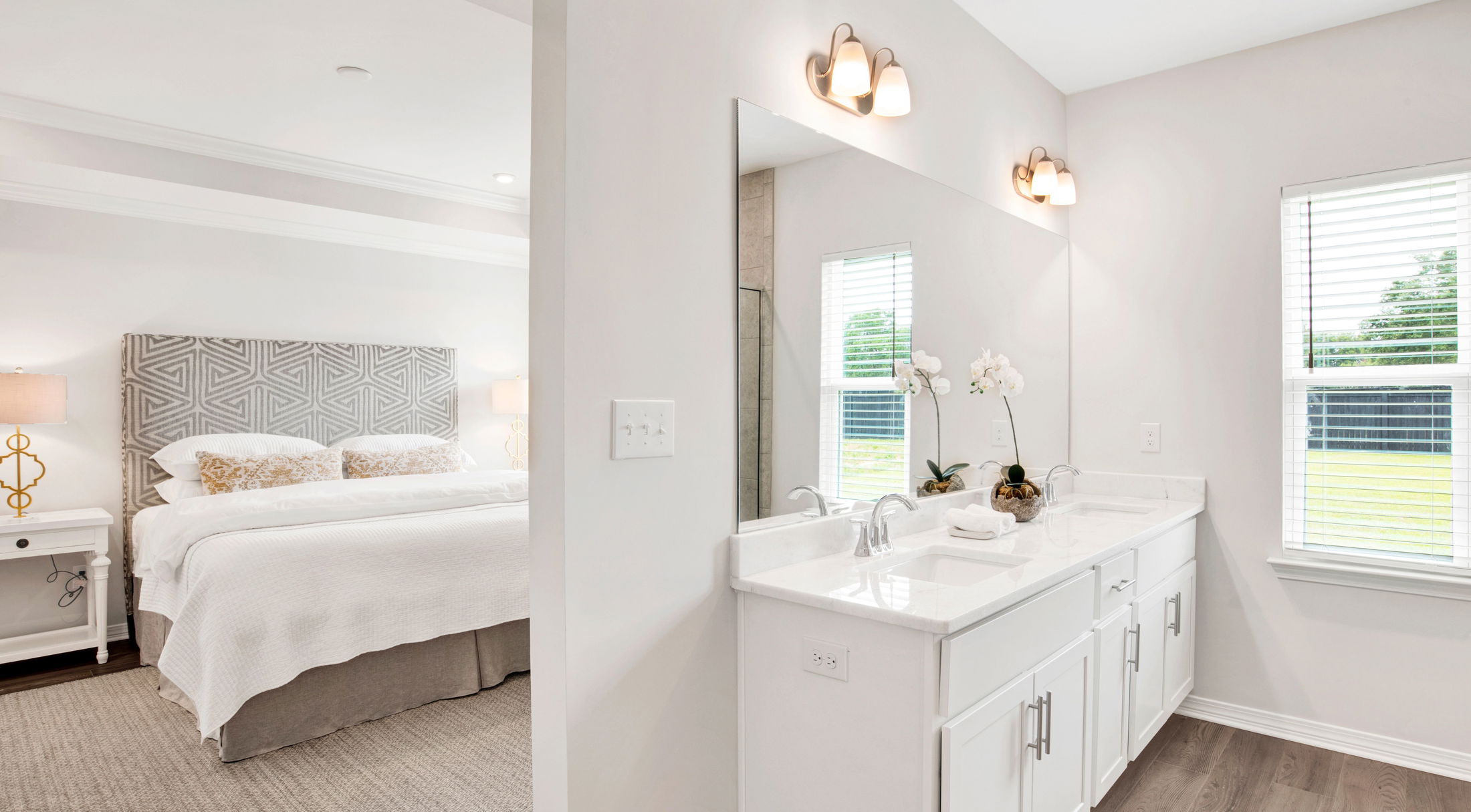 Modern bedroom with grey and white decor featuring an adjacent en-suite bathroom with a large mirror and double vanity.