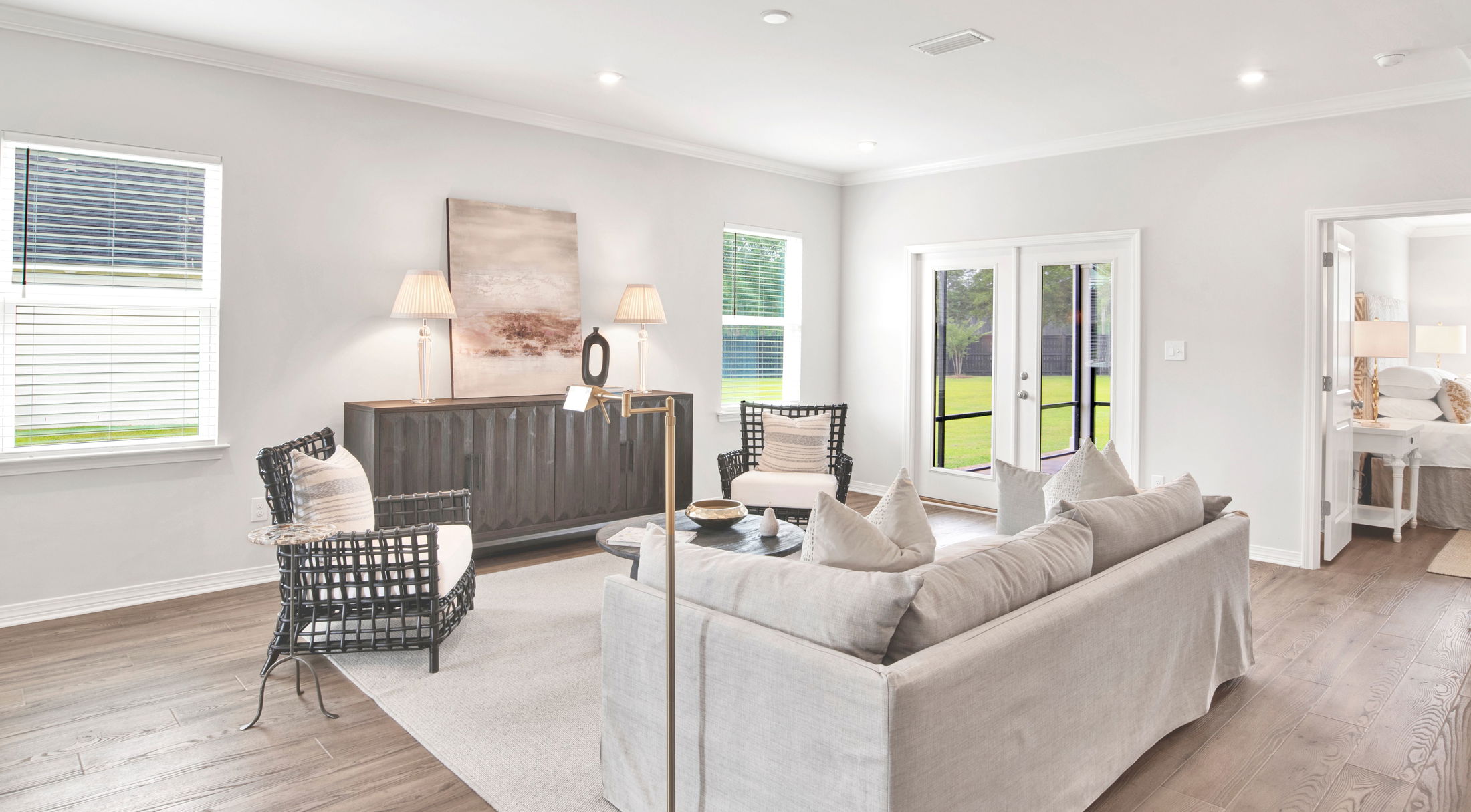 Elegant and bright living room with modern decor, featuring a beige sofa, accent chairs, and large windows overlooking a green yard.