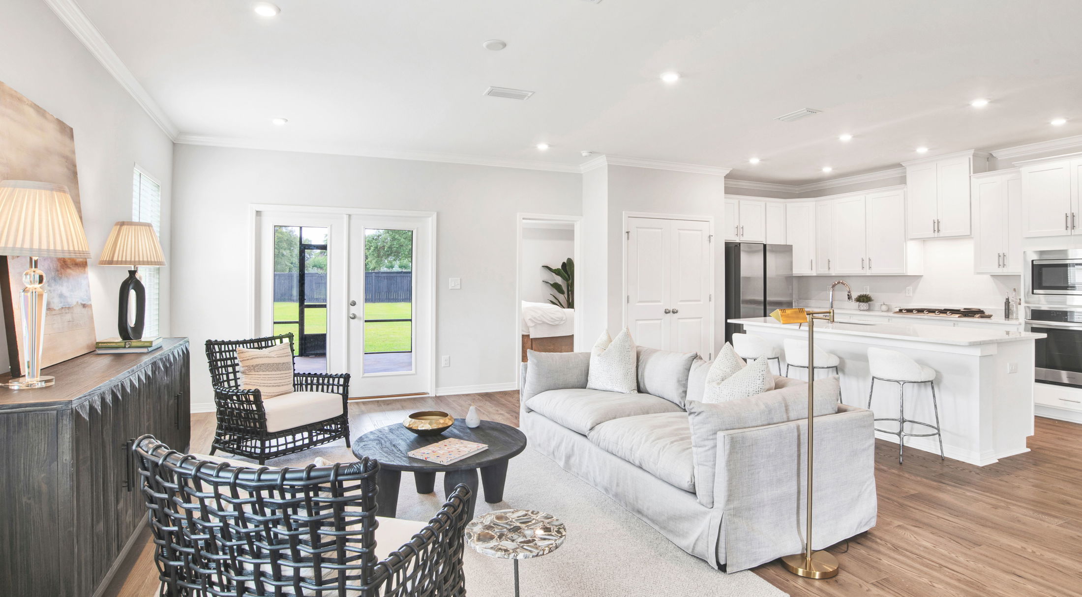 Modern open-concept living room and kitchen with white cabinetry, a gray sofa, and stylish wicker chairs.