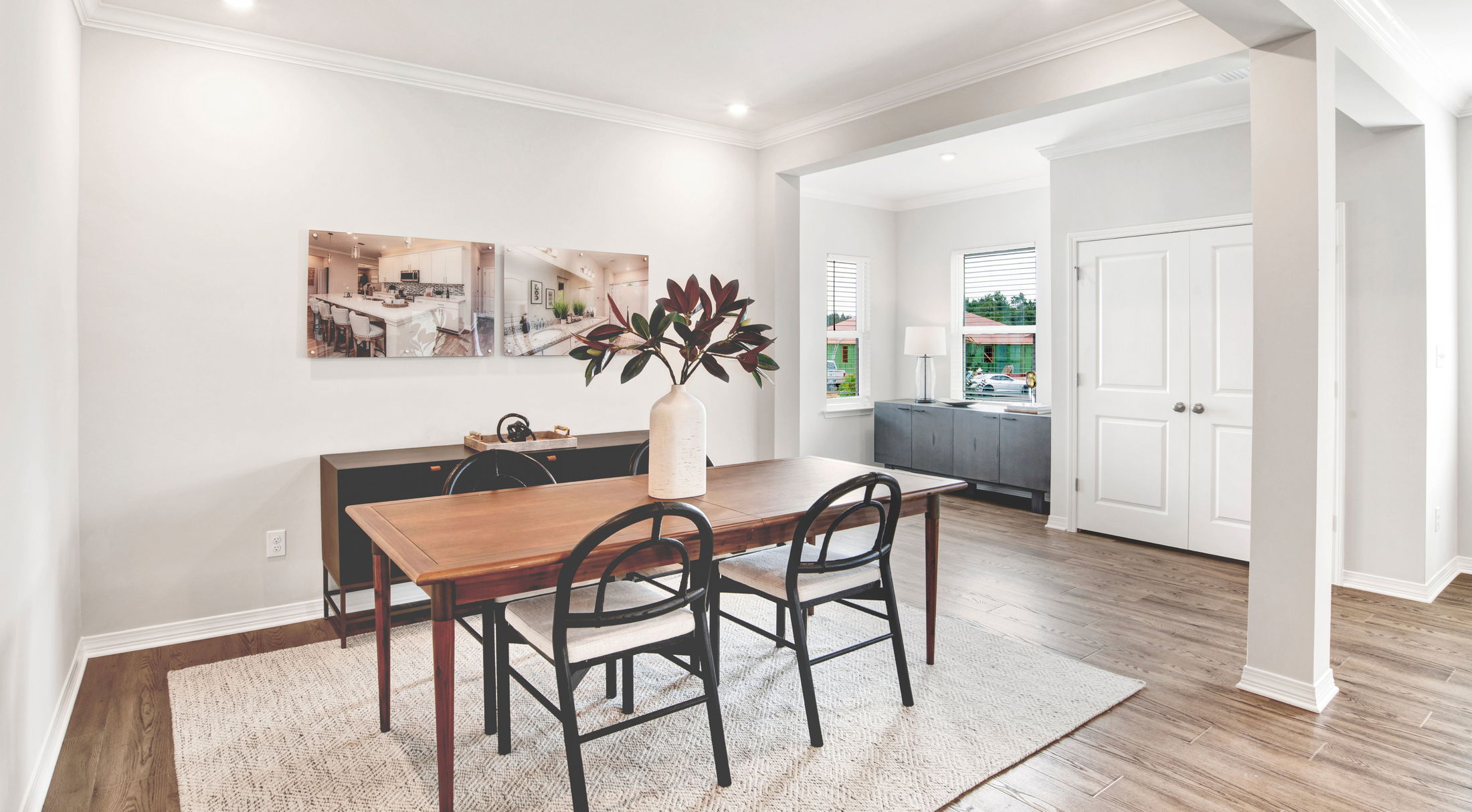 Sleek dining room with a wooden table, black chairs, and a decorative plant, accented by modern artwork on white walls.