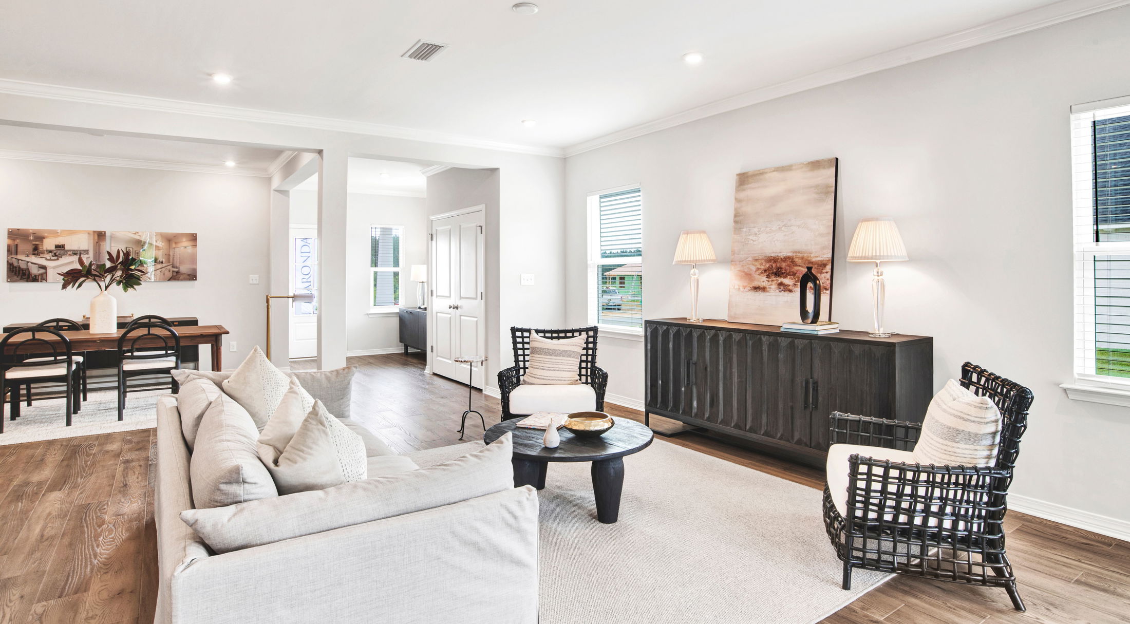 Modern living room with a cozy sofa, wicker chairs, and a wooden dining table, featuring contemporary decor and hardwood flooring.