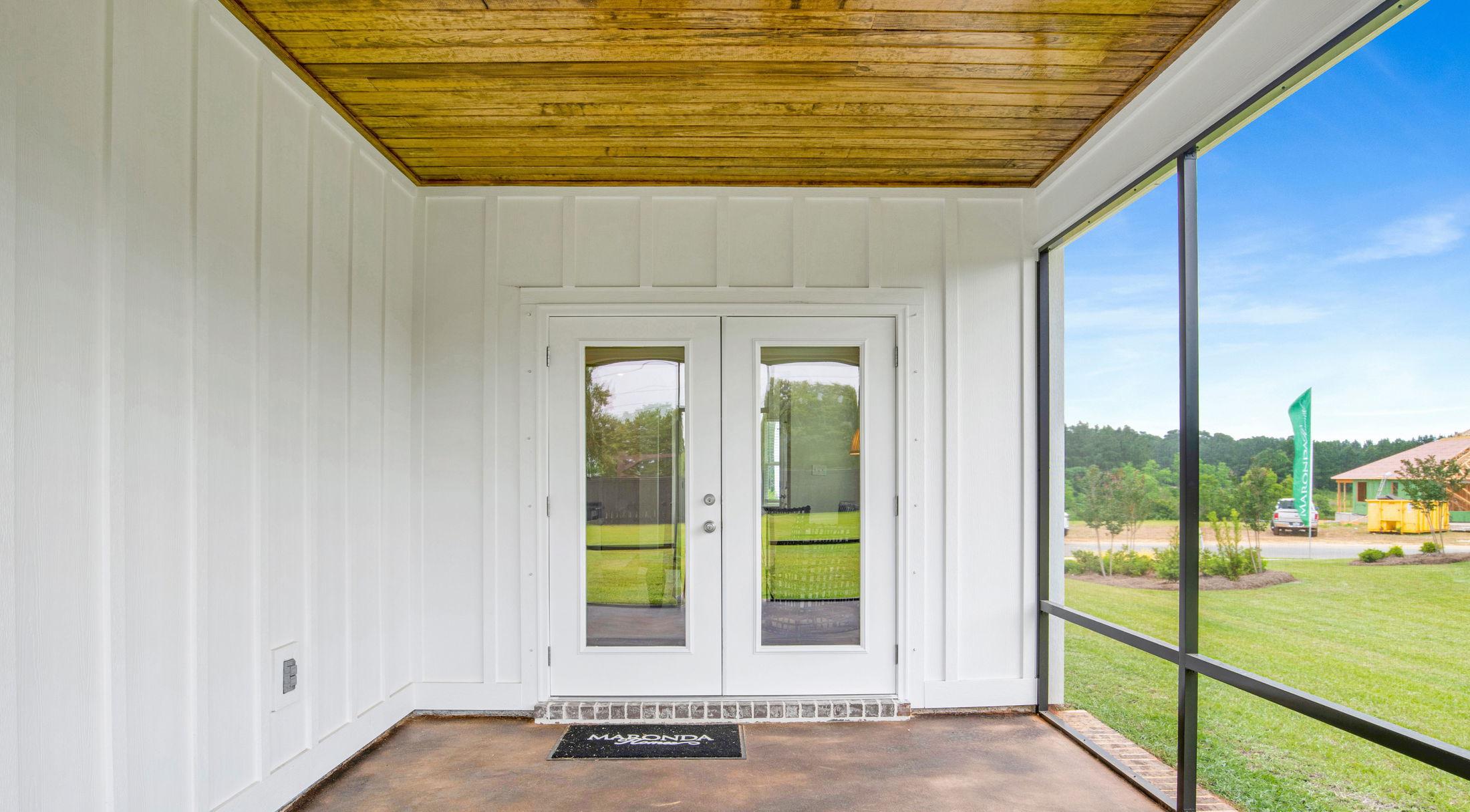 Screened-in porch with white double doors, wood ceiling, and exterior garden view, highlighting a modern, welcoming home entrance.