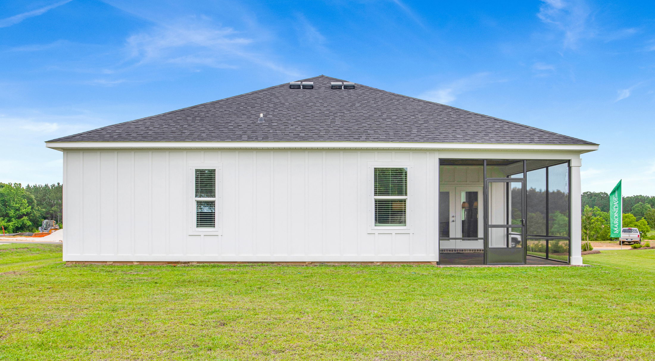 Rear view of a modern white house with a screened porch and large green lawn under a clear blue sky.