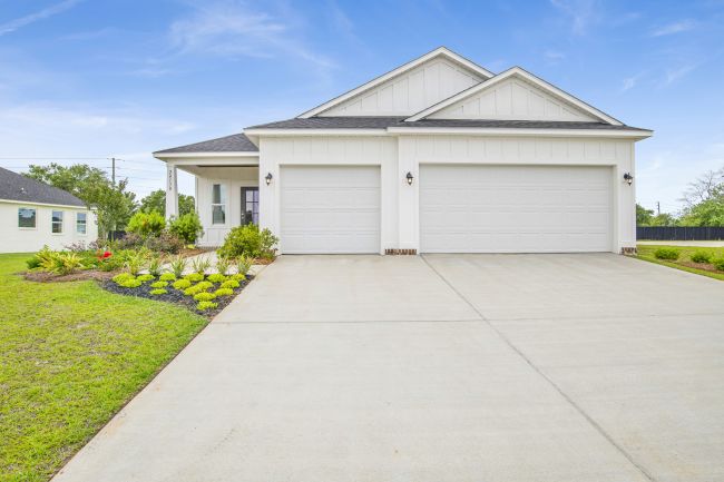 Modern suburban home with a large driveway, white exterior, and landscaped front yard under a clear blue sky.