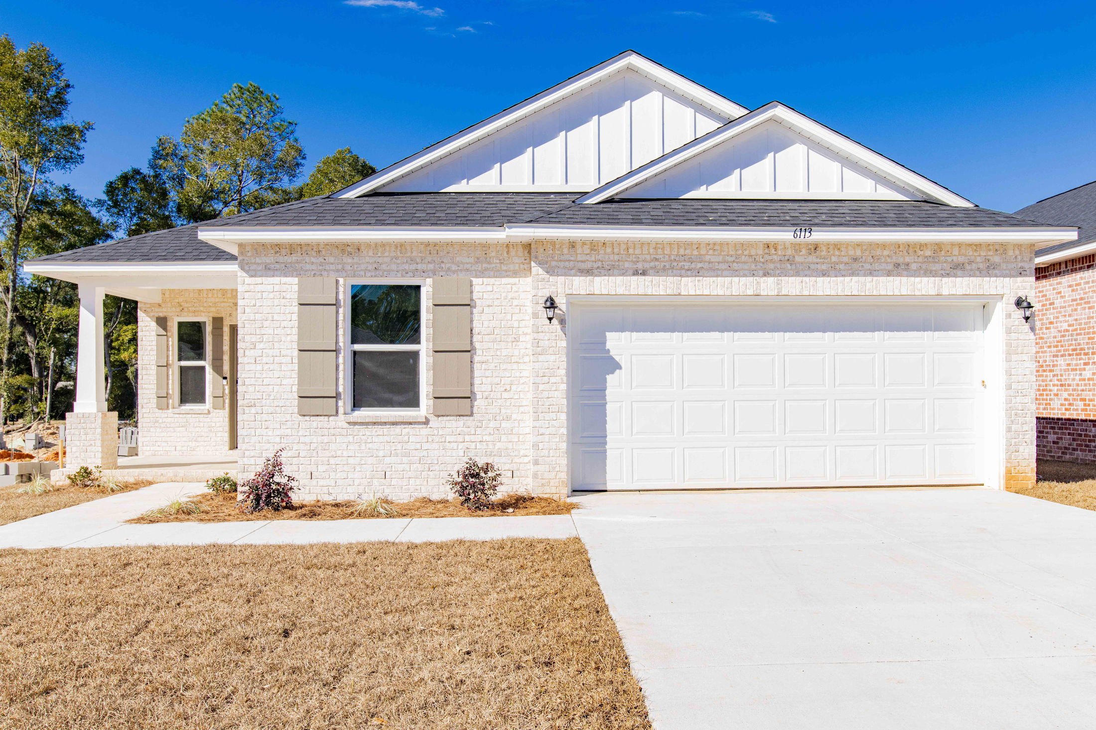 Newly built white brick suburban house with a two-car garage and manicured lawn under a clear blue sky.