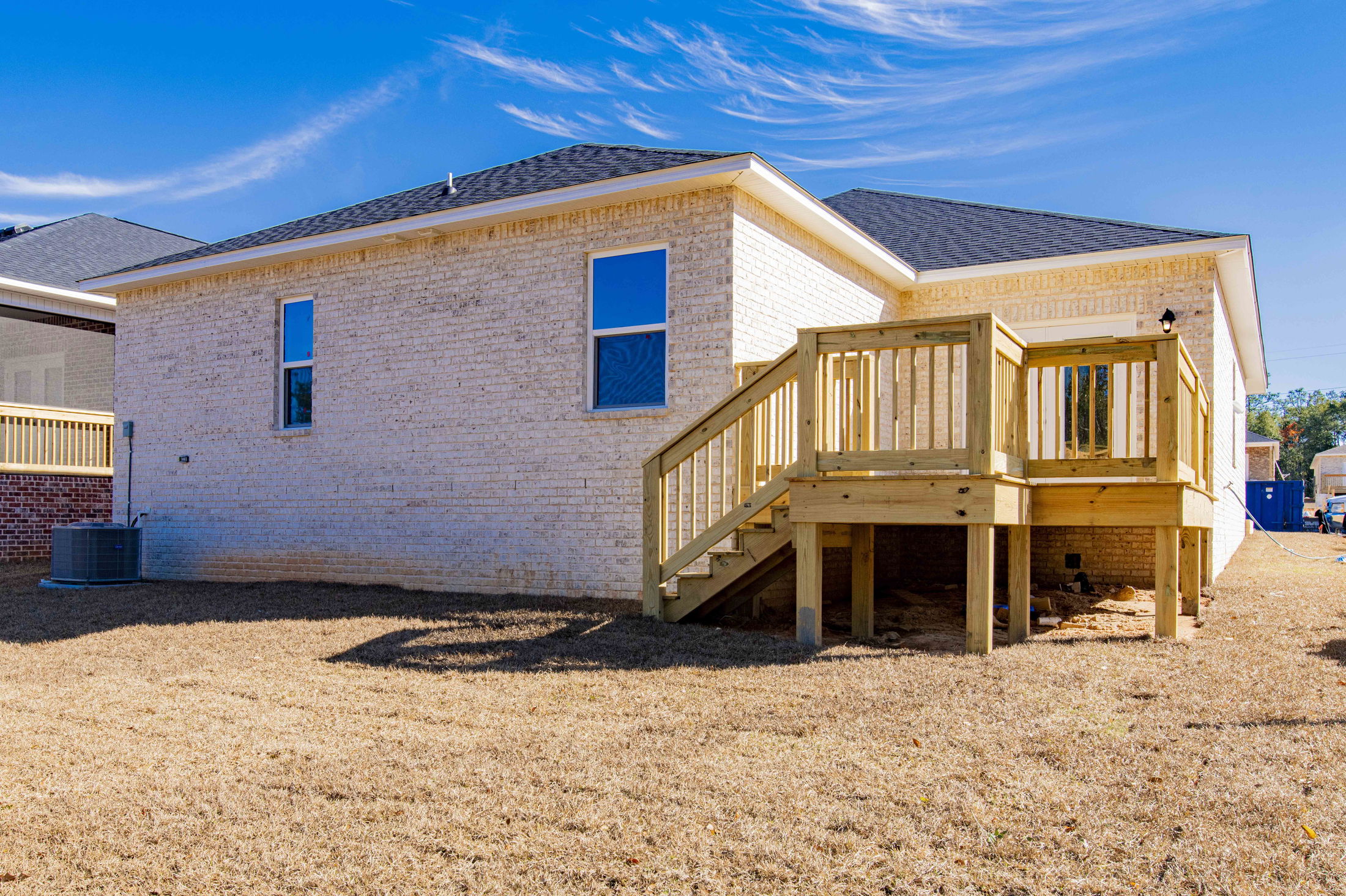 Backyard view of a modern single-story brick house with a small wooden deck and staircase.