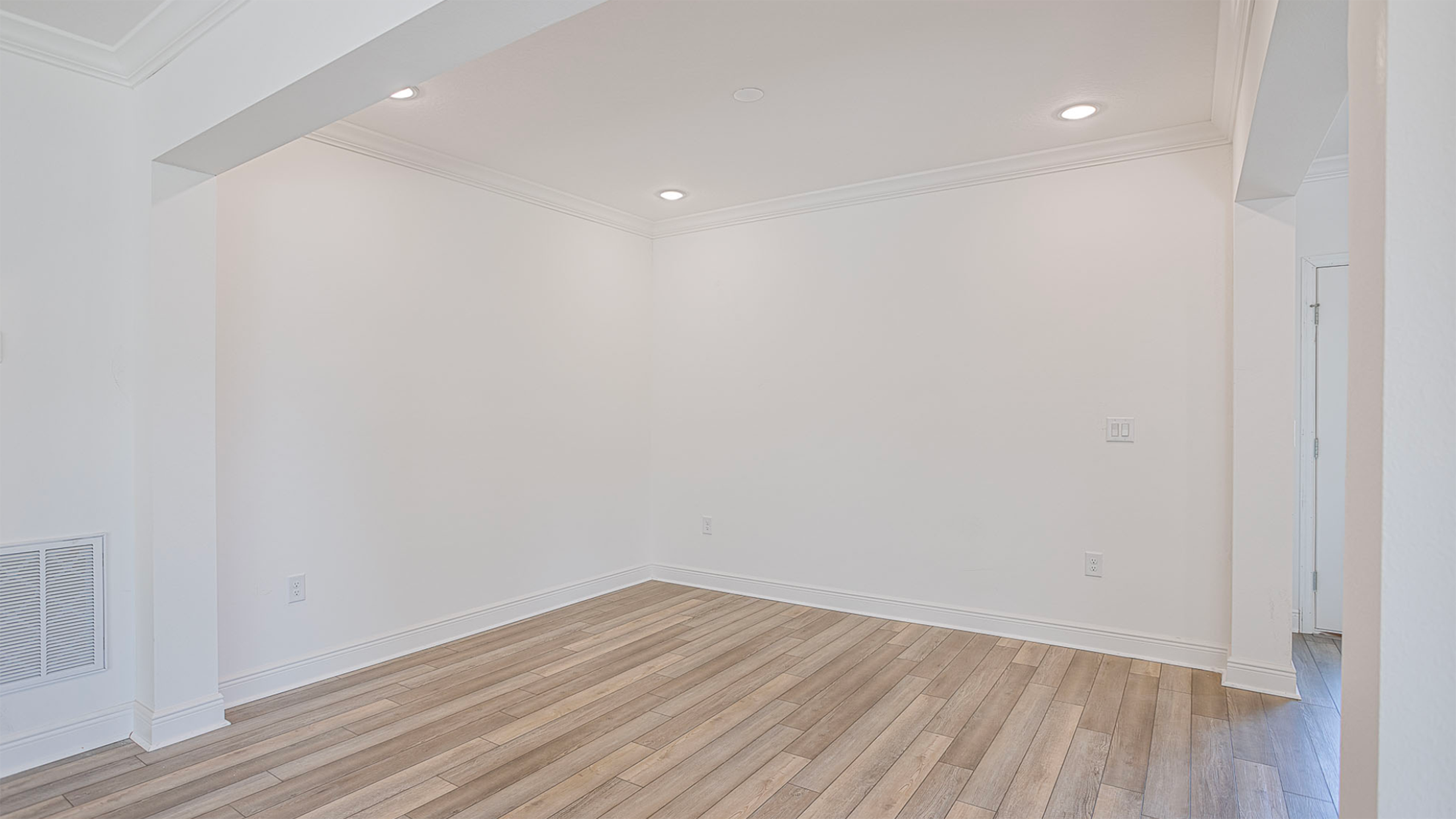 Empty room with light wooden flooring, white walls, and recessed lighting, ideal for home interior design.