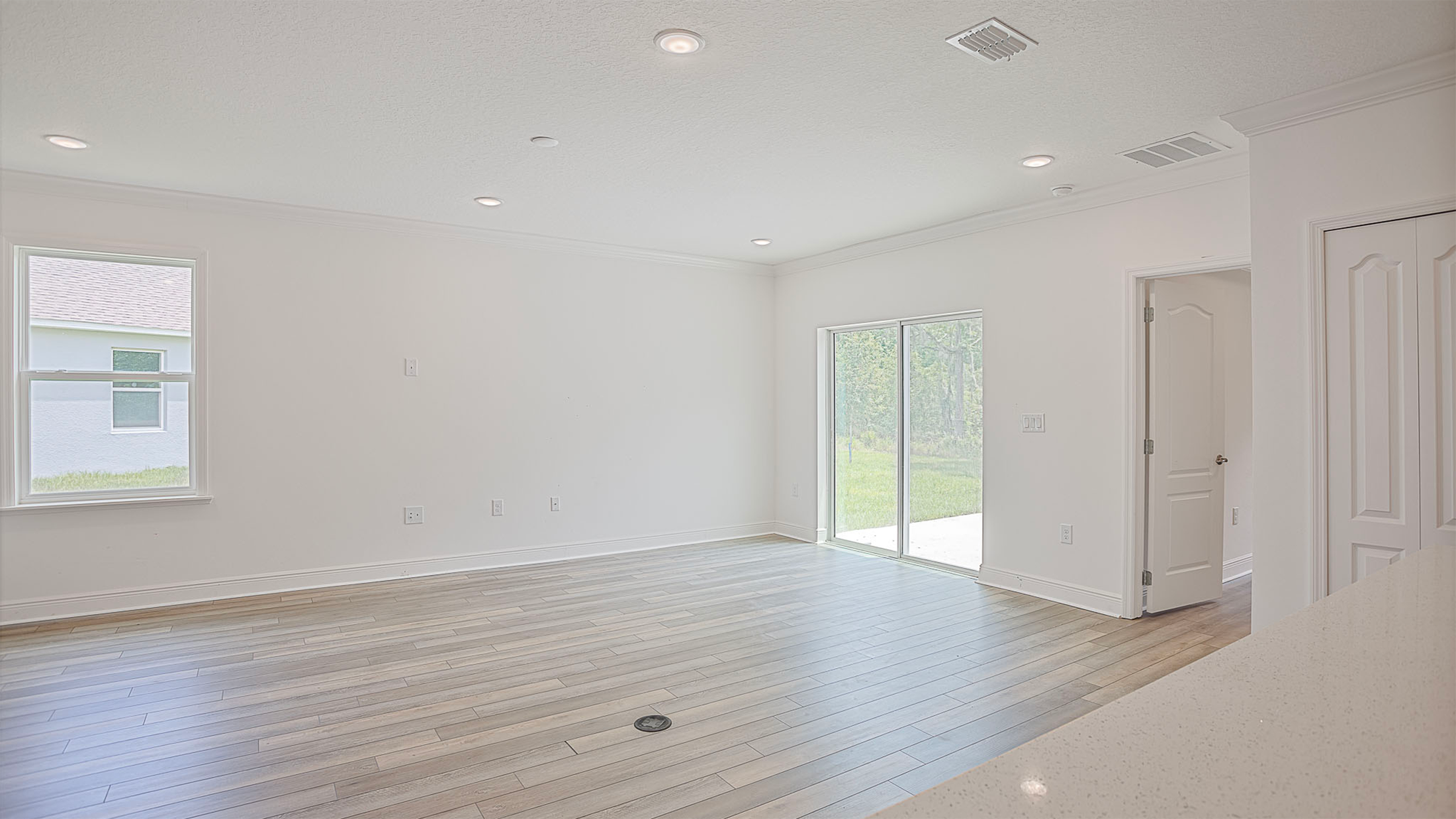 Modern, unfurnished living room with hardwood floors, white walls, and large sliding glass doors leading to a grassy backyard.