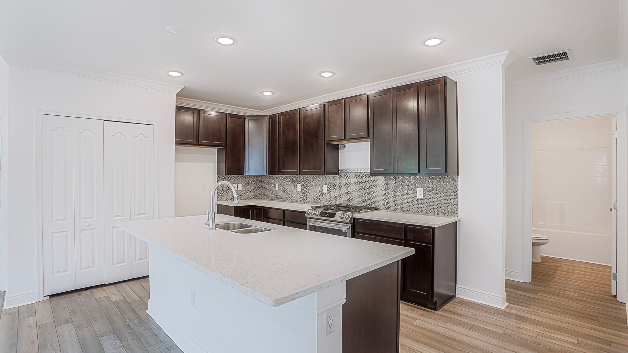 Modern kitchen interior with dark wood cabinets, white quartz countertops, and a mosaic tile backsplash.