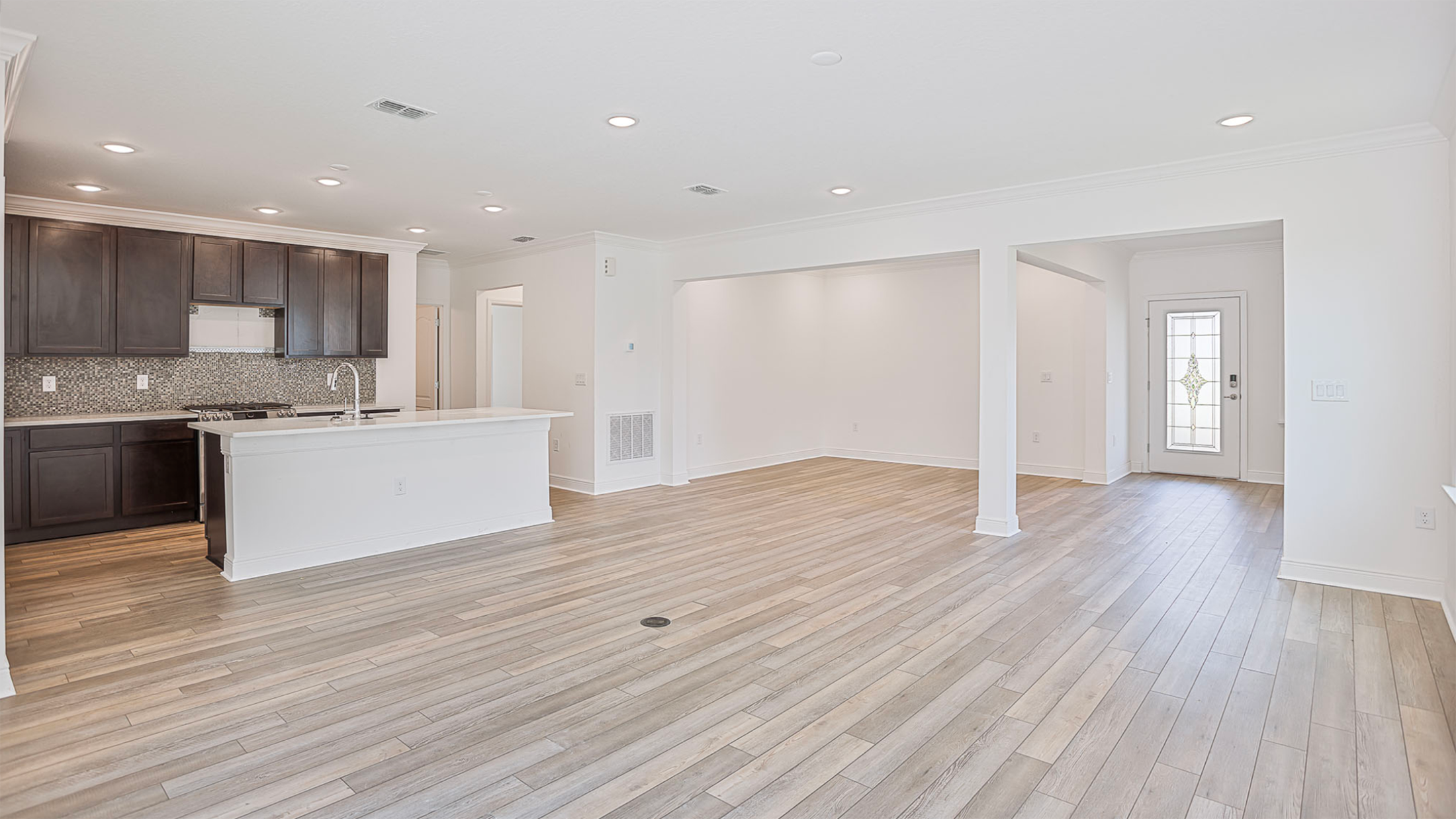 Modern open-concept living space with hardwood floors, featuring a kitchen with dark cabinets and mosaic backsplash.