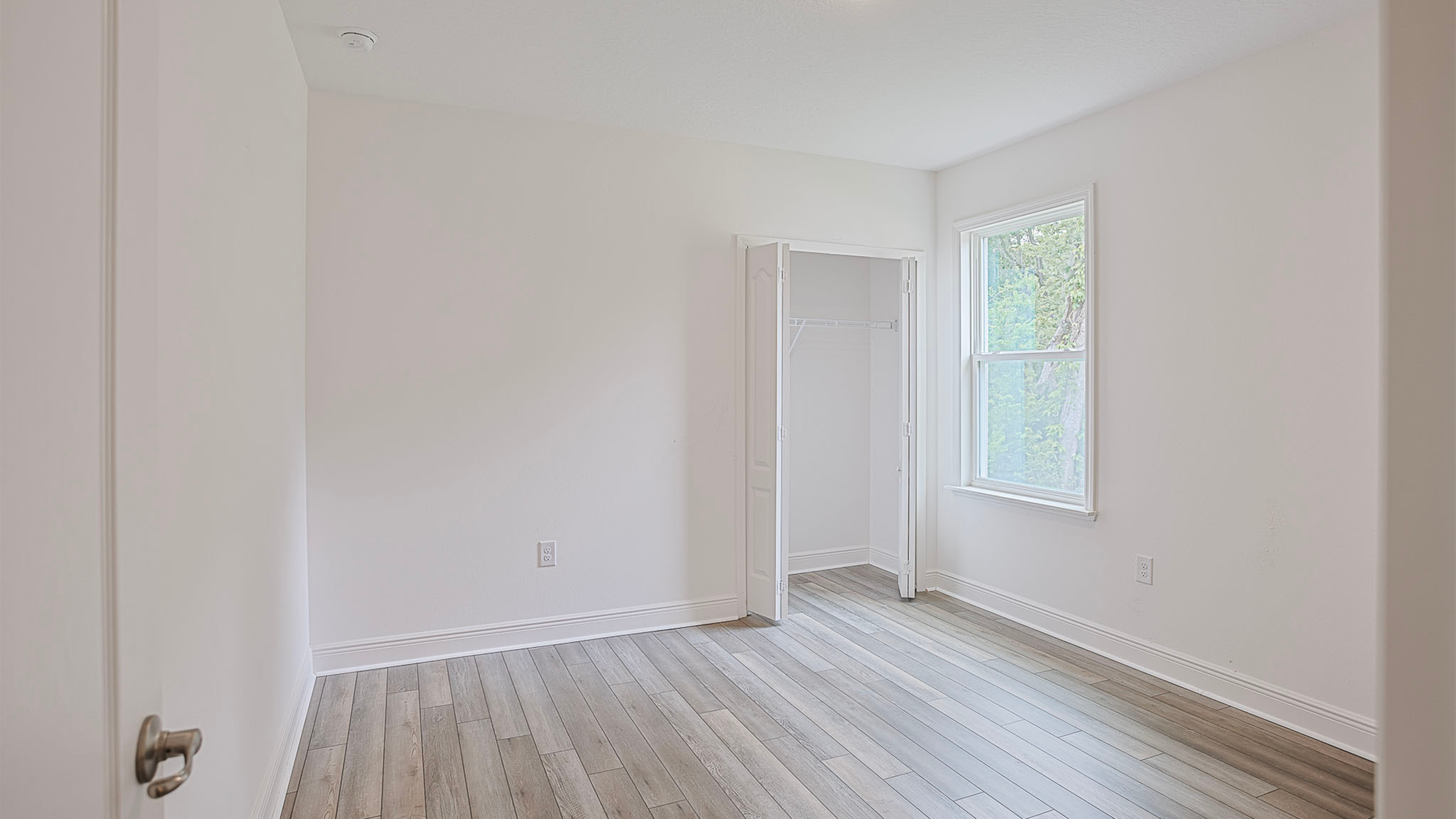 Empty room with light hardwood flooring, a small closet, and a window providing natural light.
