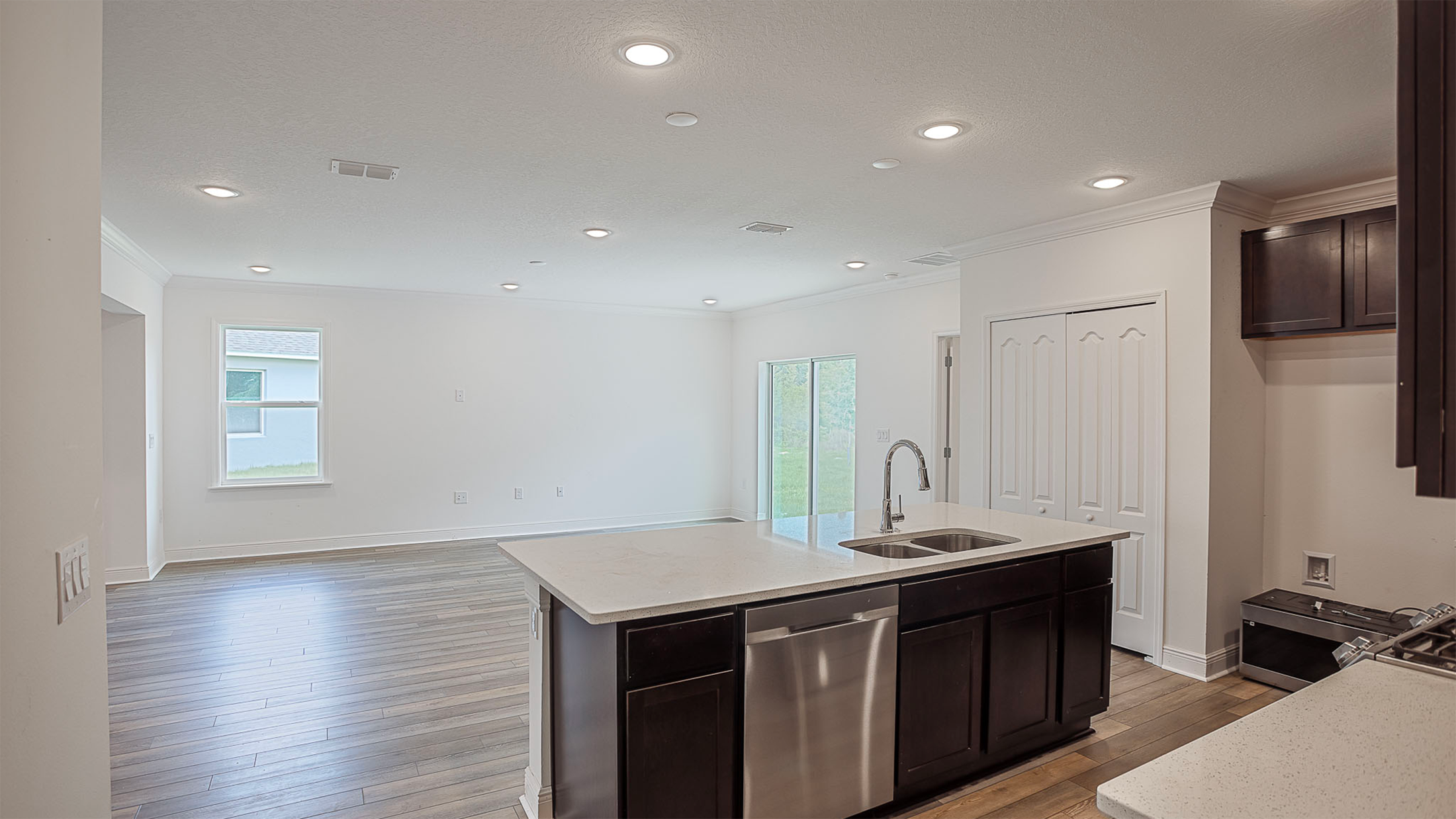 Modern open-plan kitchen and living area with wooden floors, recessed lighting, and an island with a built-in sink.