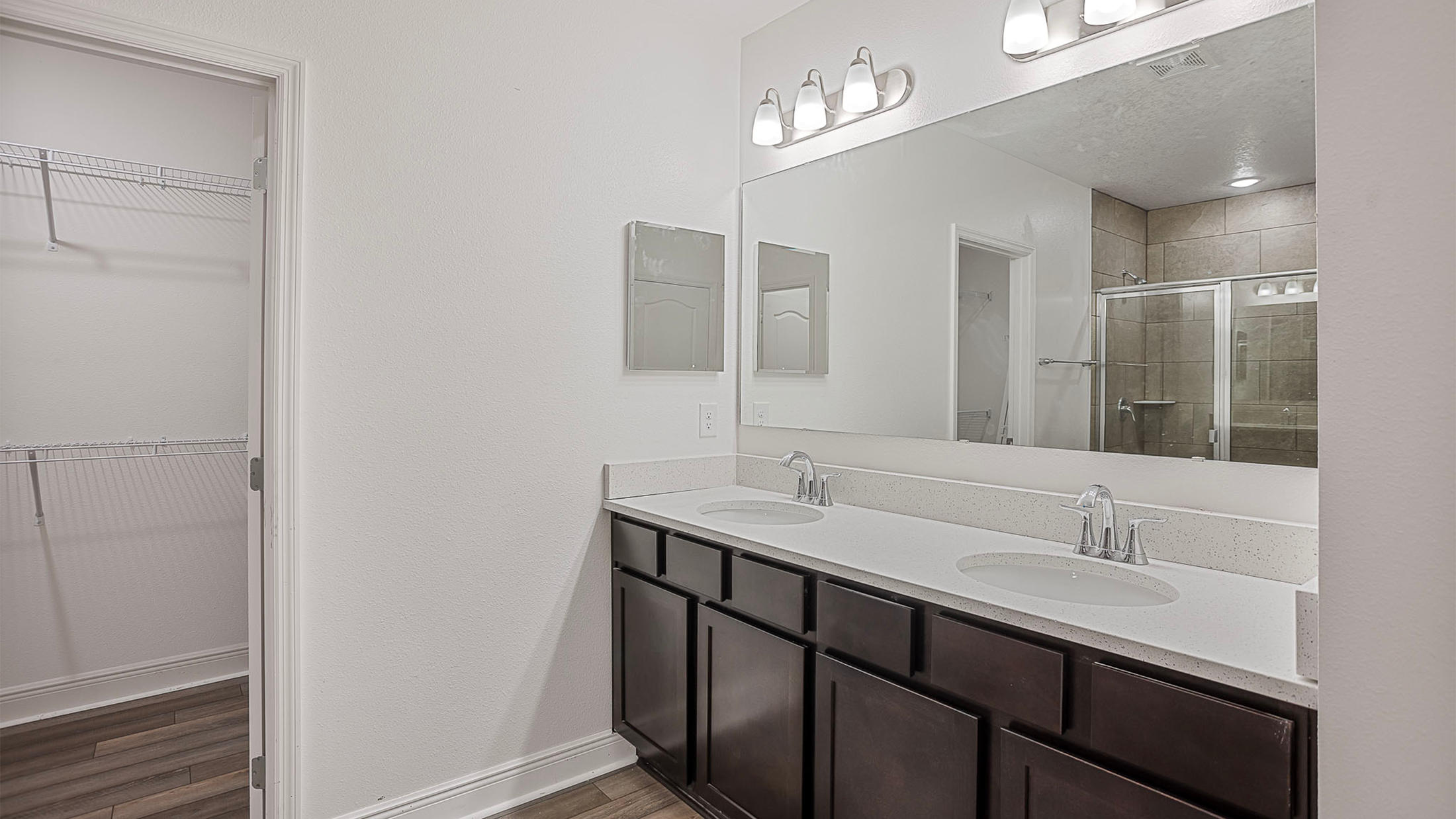 Modern bathroom with dark wood cabinets, double vanity, large mirror, and glass shower.