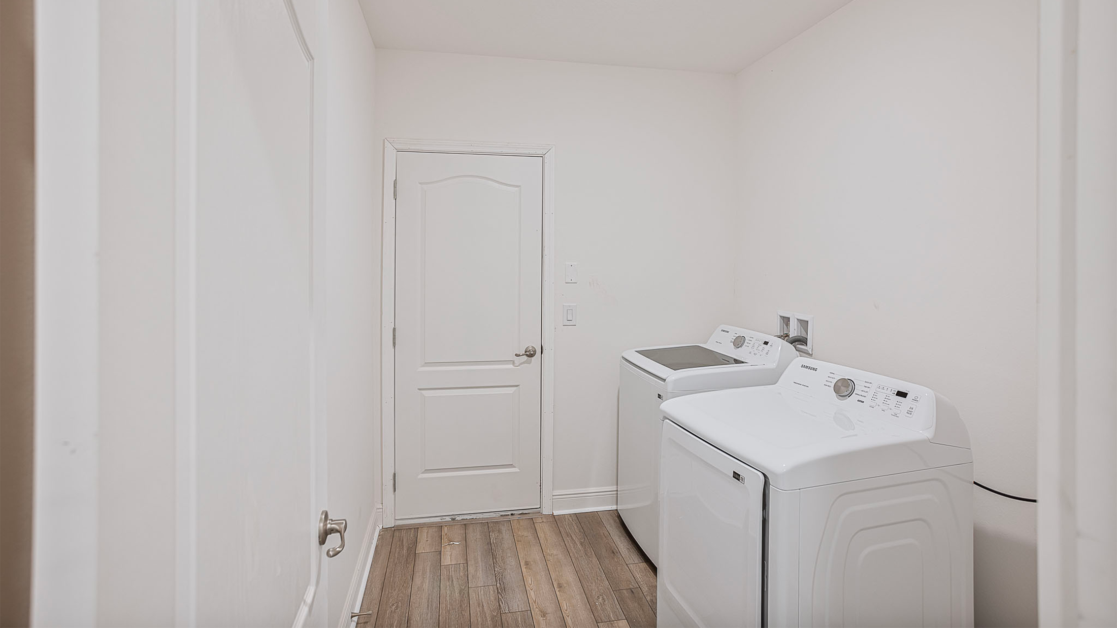 Modern laundry room with a Samsung washer and dryer set on a wooden floor next to a white door.