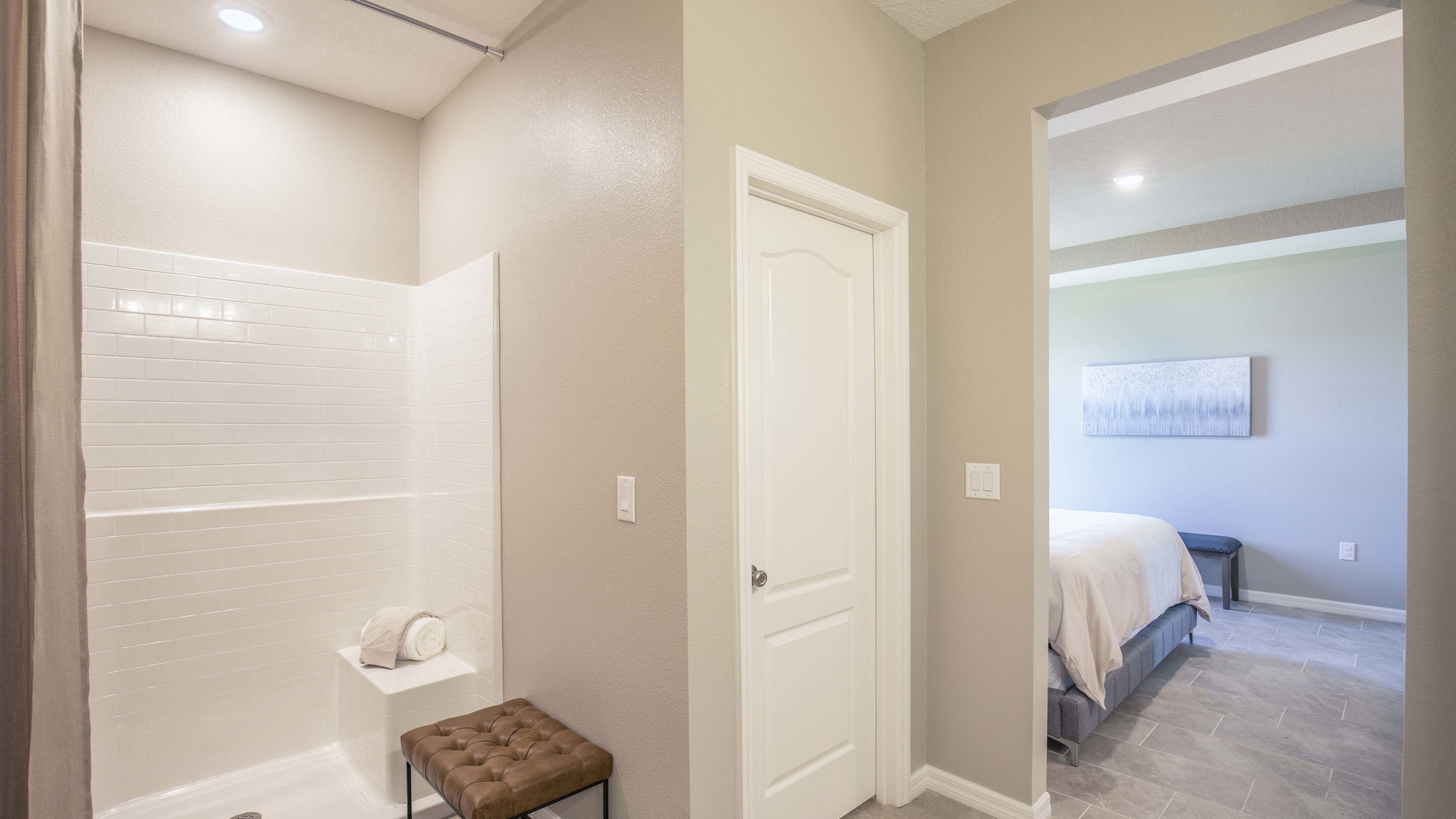 Modern bathroom with a white tiled shower and adjacent bedroom visible through an open doorway.