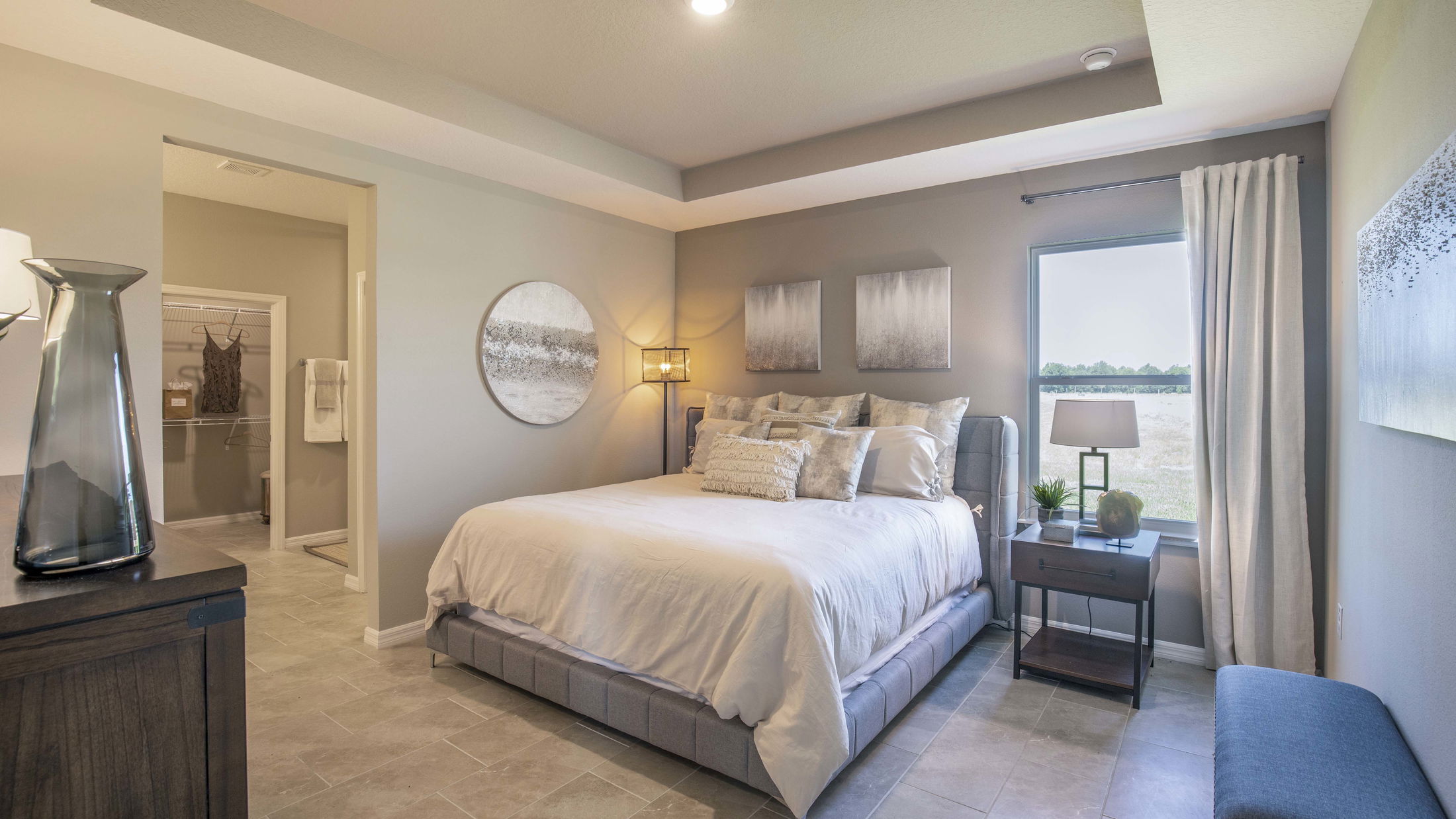 Modern bedroom with a neatly made bed, elegant decor, and a view through a large window, providing a serene and inviting atmosphere.