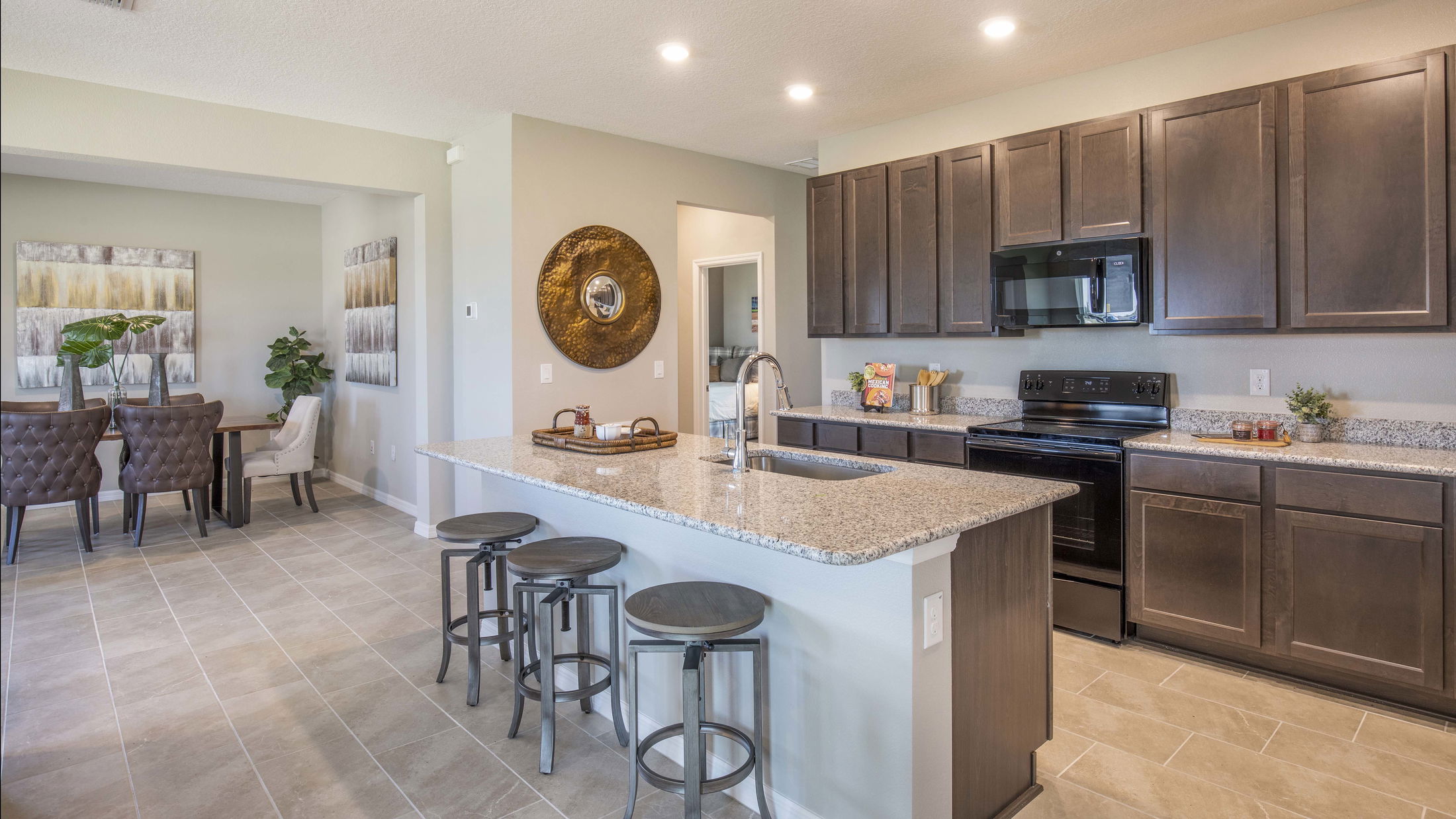 Modern kitchen interior with granite countertops, dark wood cabinets, and an open dining area featuring stylish decor and bar stools.