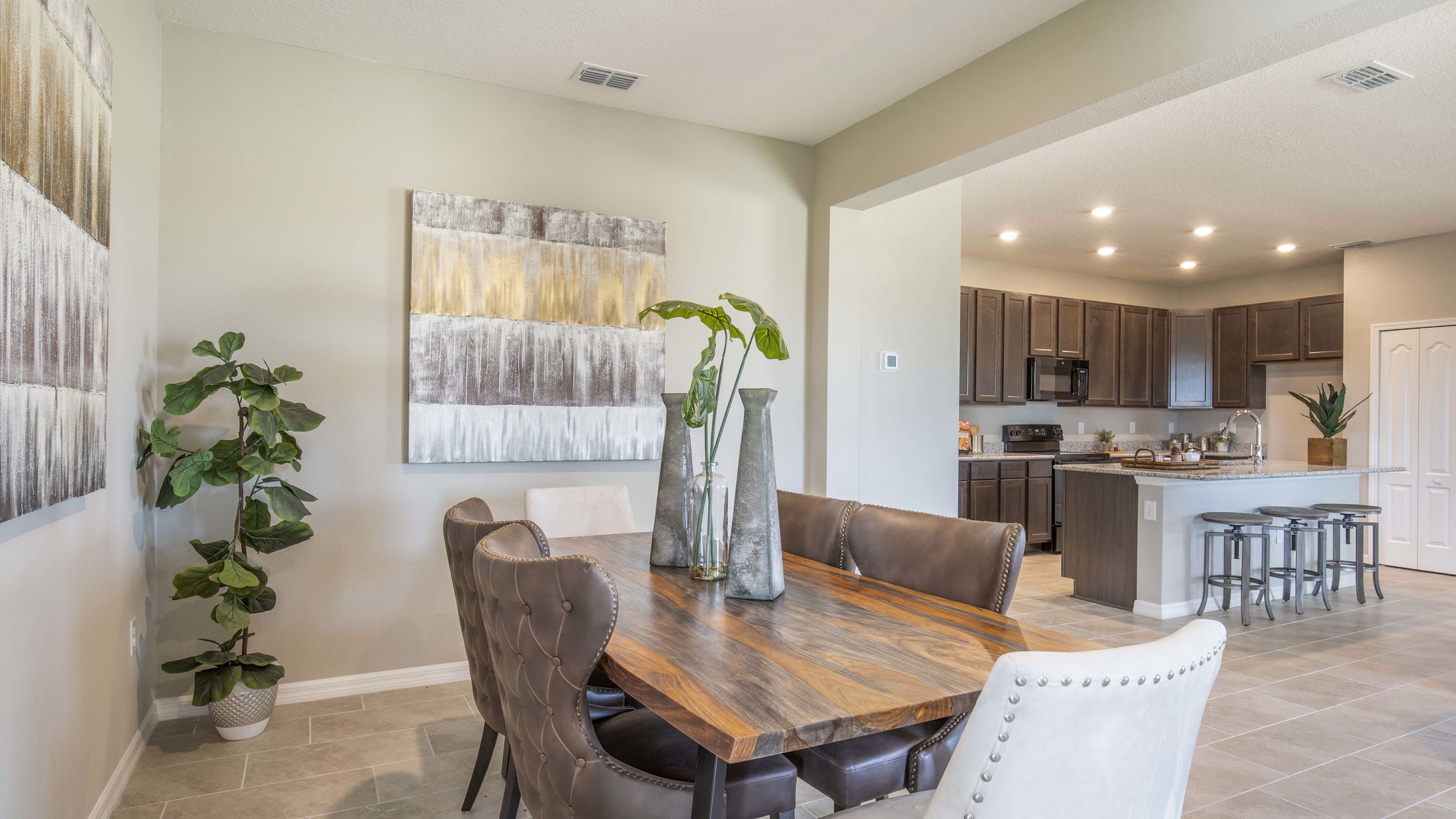 Modern dining room with a wooden table, brown leather chairs, and a view of the open kitchen featuring dark cabinetry and bar stools.