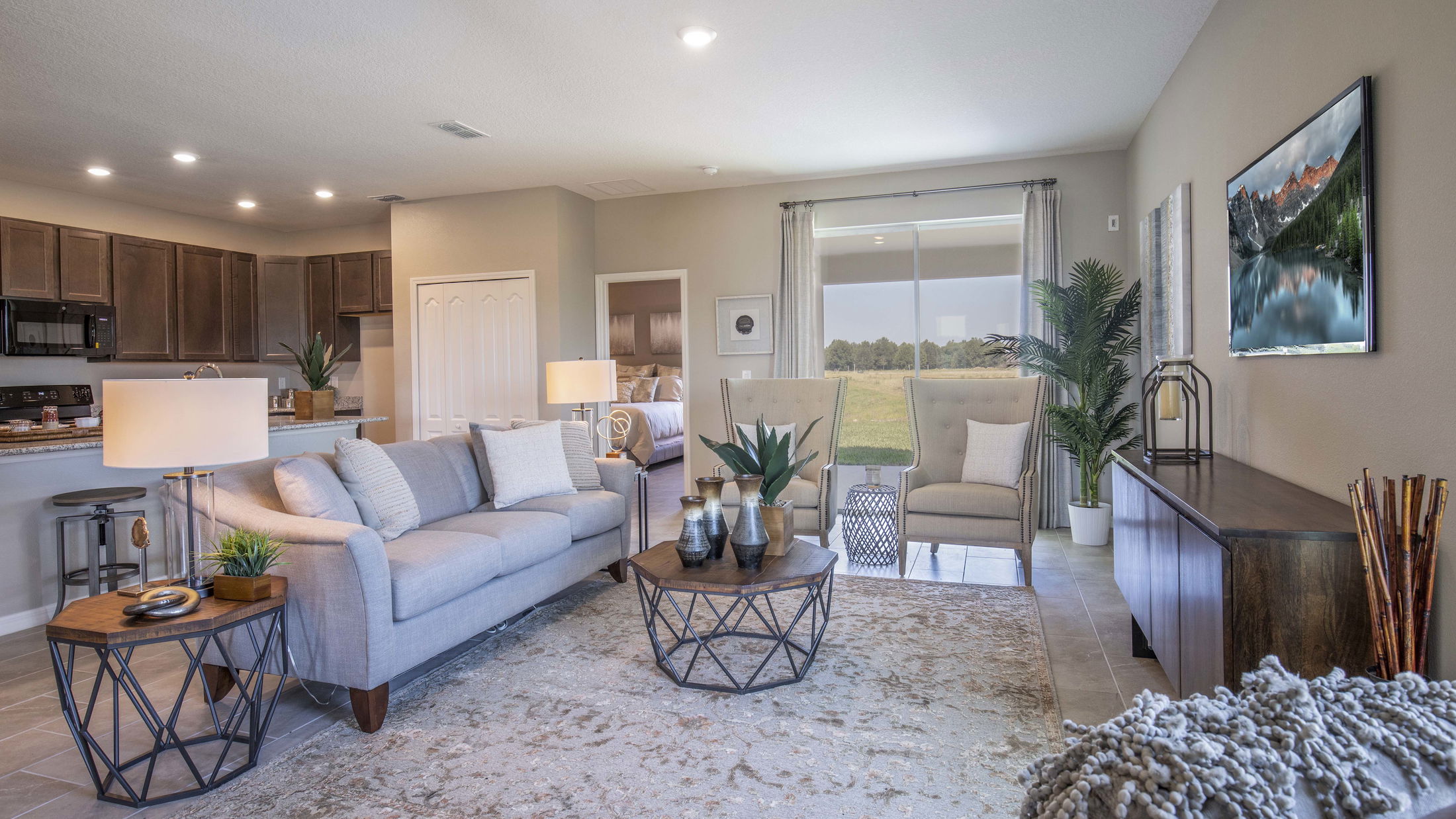 Modern living room interior with gray sofa, wooden furniture, and open view to the kitchen.