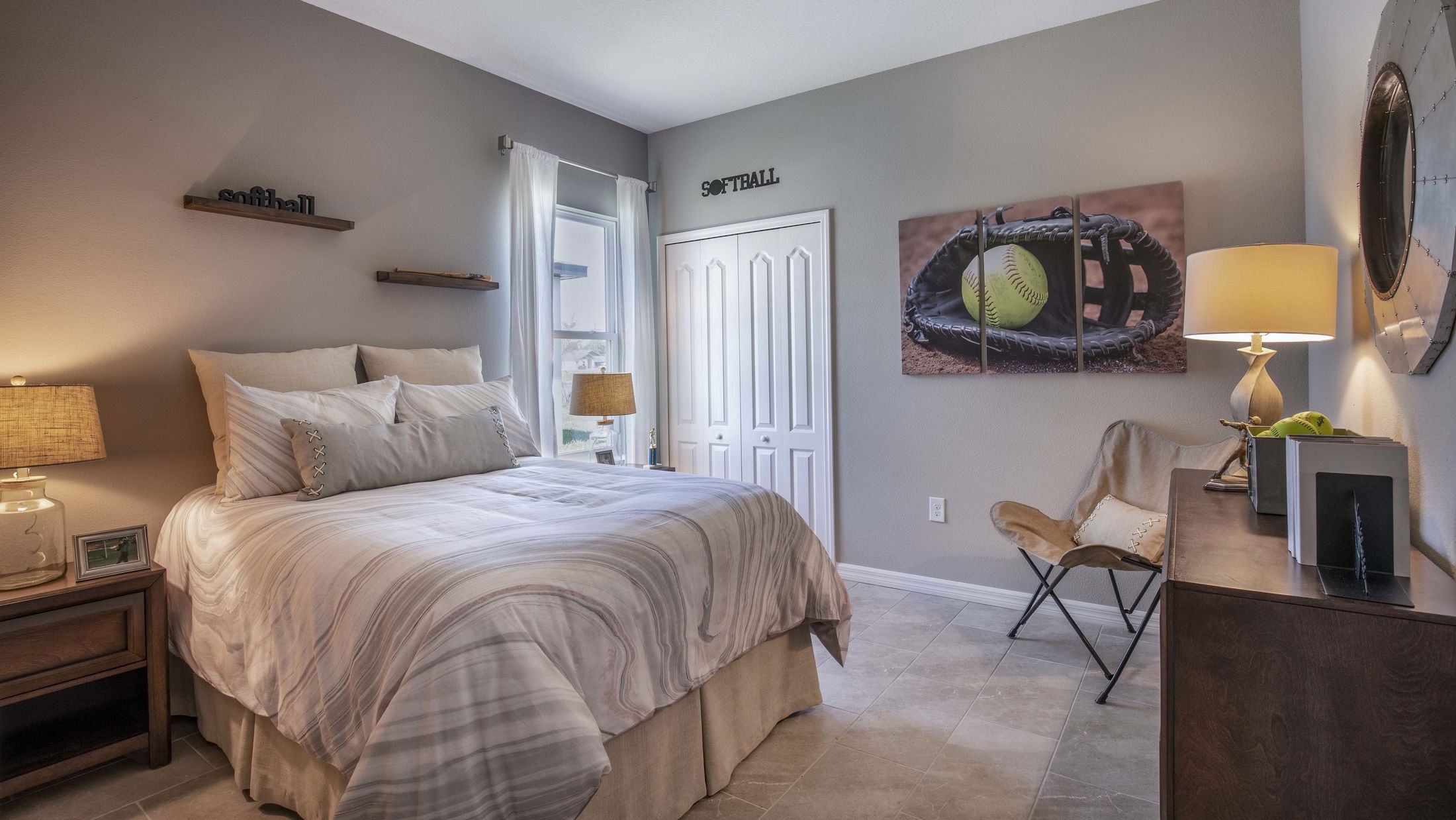 Cozy bedroom with sports-themed decor, featuring a large bed, bedside tables with lamps, and a softball glove art piece on the wall.
