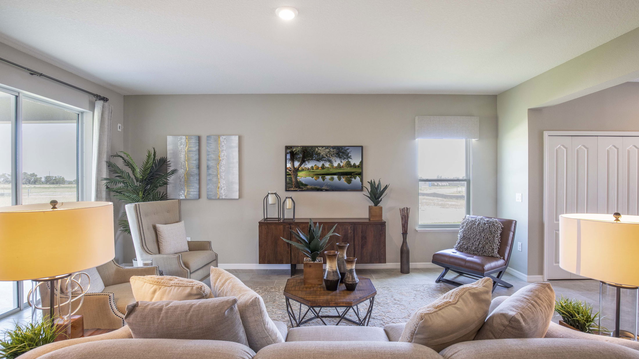 Modern living room with beige sofas, stylish decor, and large windows providing natural light.