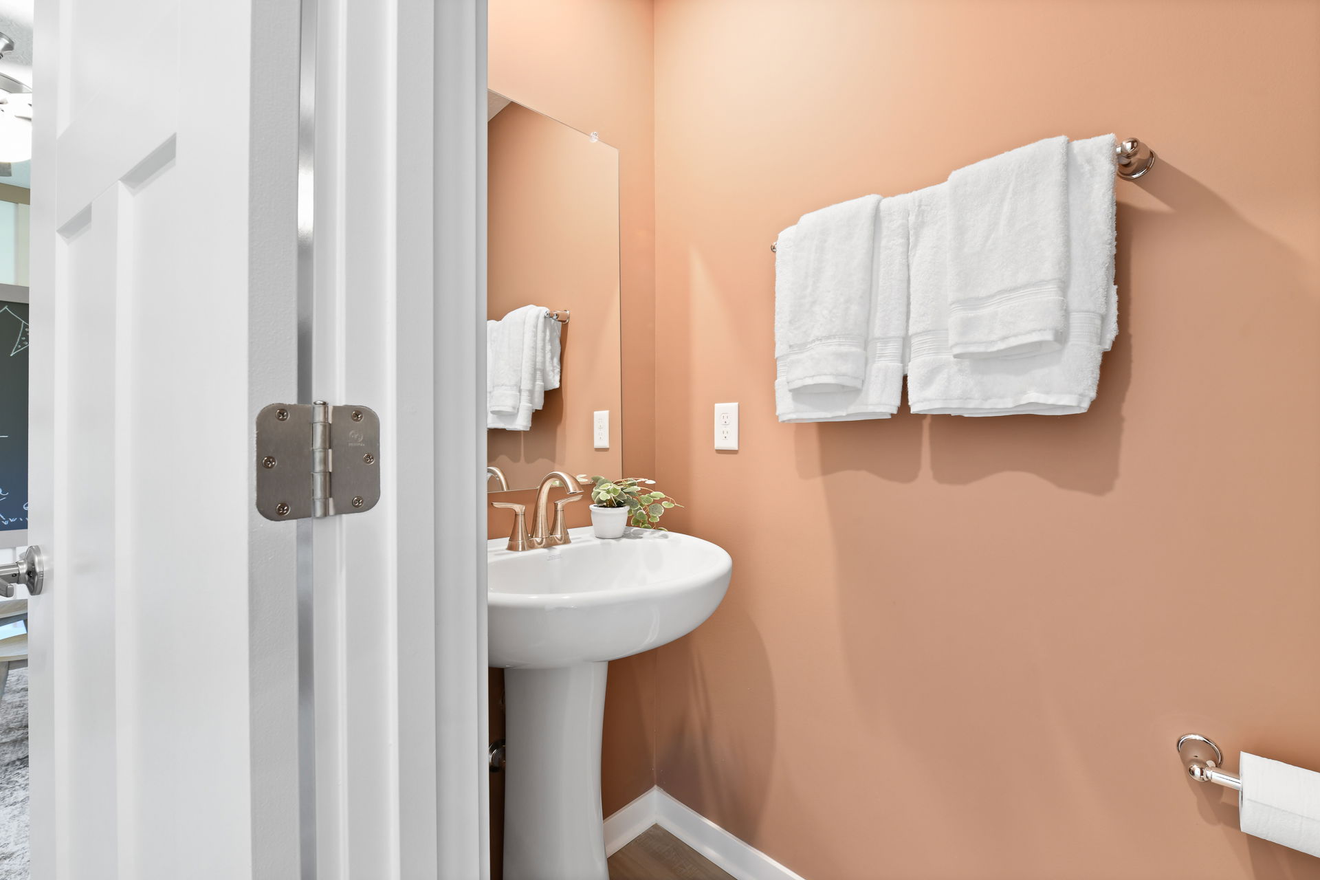 Modern bathroom with peach walls, a pedestal sink, white towels, and a small potted plant for decoration.