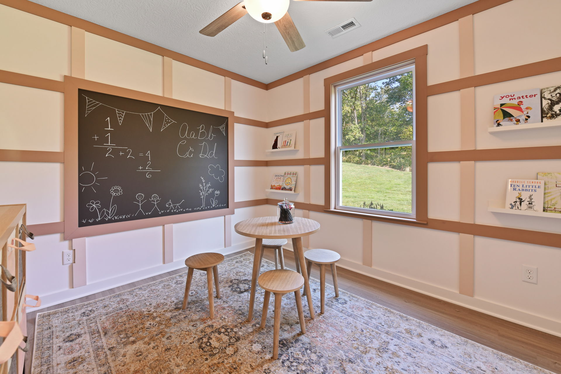 Children's playroom with a chalkboard and educational decor featuring a round wooden table and four stools.