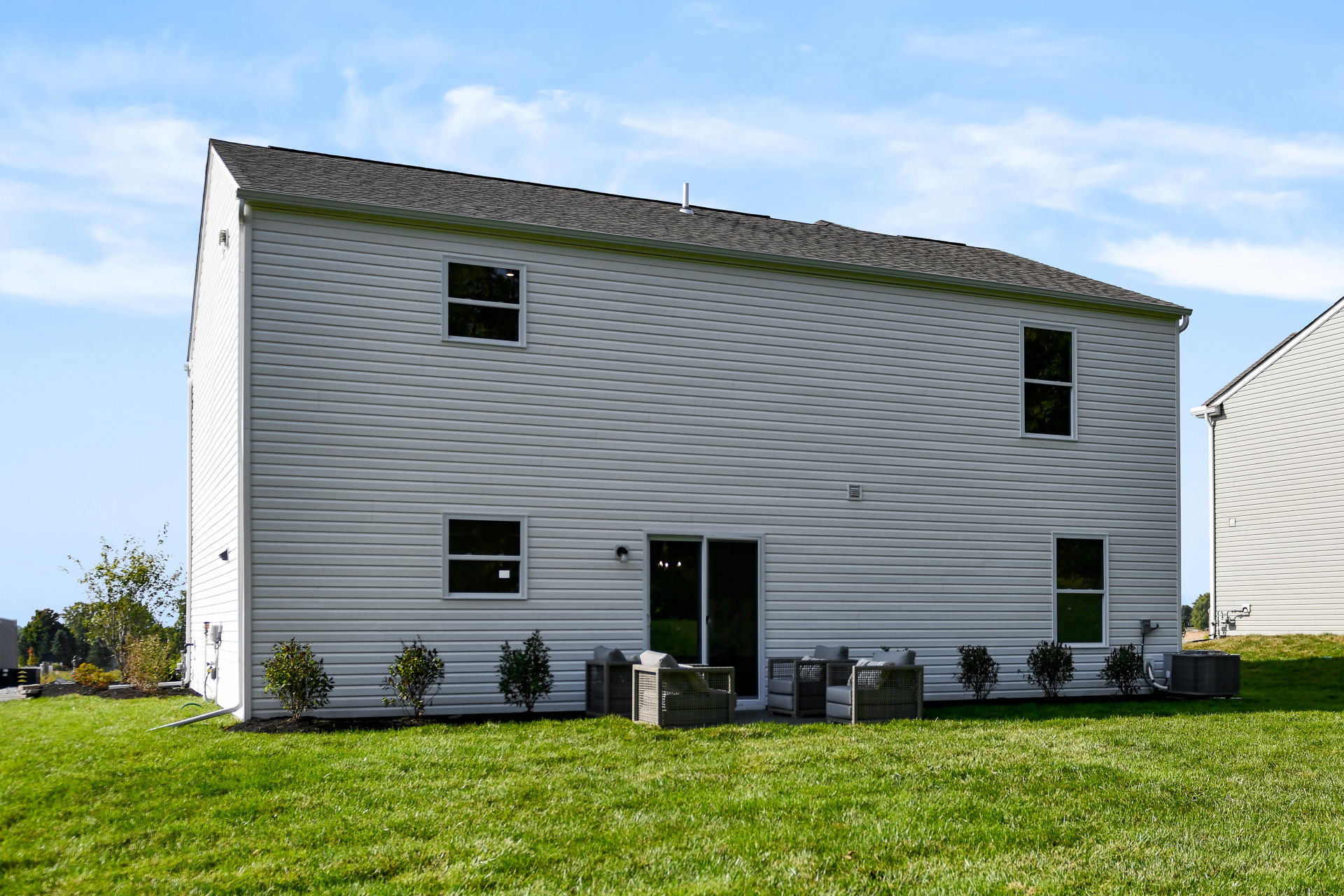 Back view of a modern two-story house with vinyl siding and a neatly landscaped backyard under a clear blue sky.