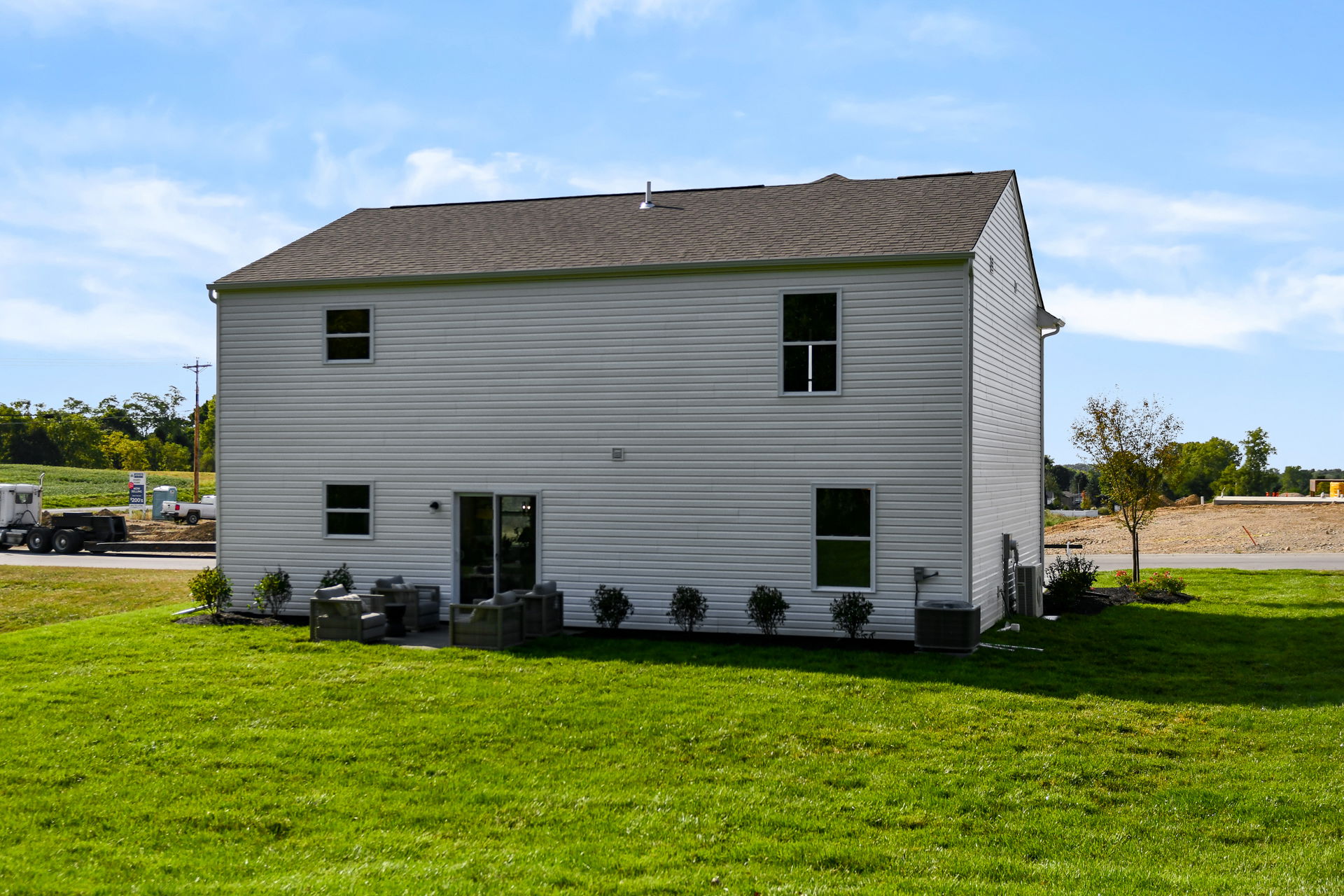 Backyard view of a modern two-story house with a patio and green lawn under a clear blue sky.