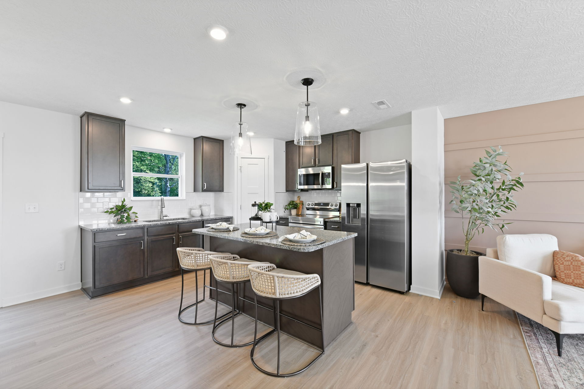 Modern kitchen with dark cabinets, an island with woven stools, stainless steel appliances, and stylish lighting fixtures.
