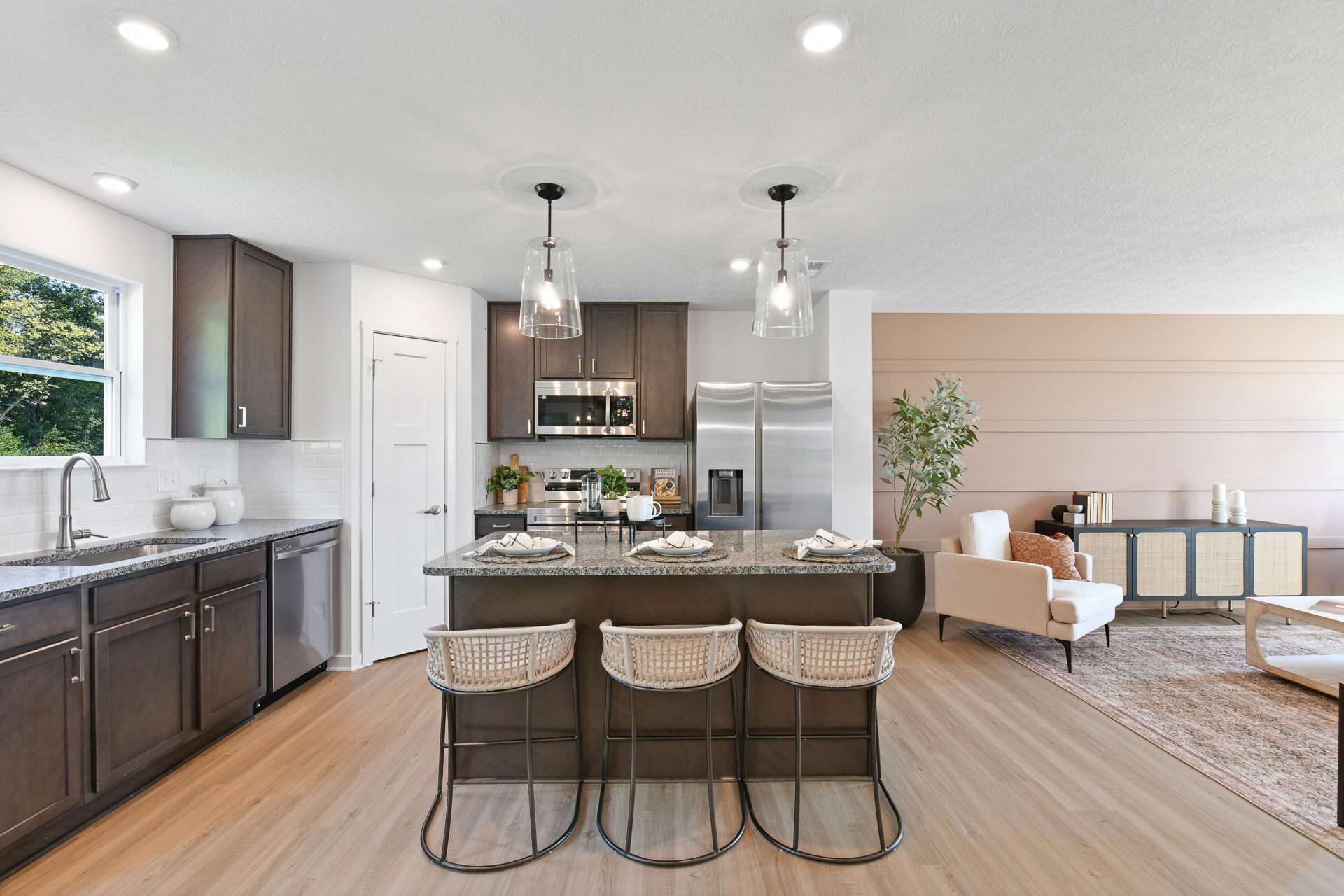 Modern kitchen and living room with dark cabinetry, stainless steel appliances, a granite island with woven chairs, and a cozy seating area.