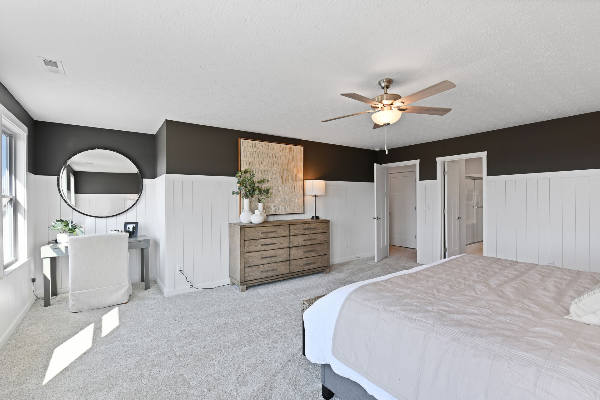 Modern bedroom interior with elegant decor, featuring a cozy bed, stylish dresser, circular mirror, and soft carpet flooring.