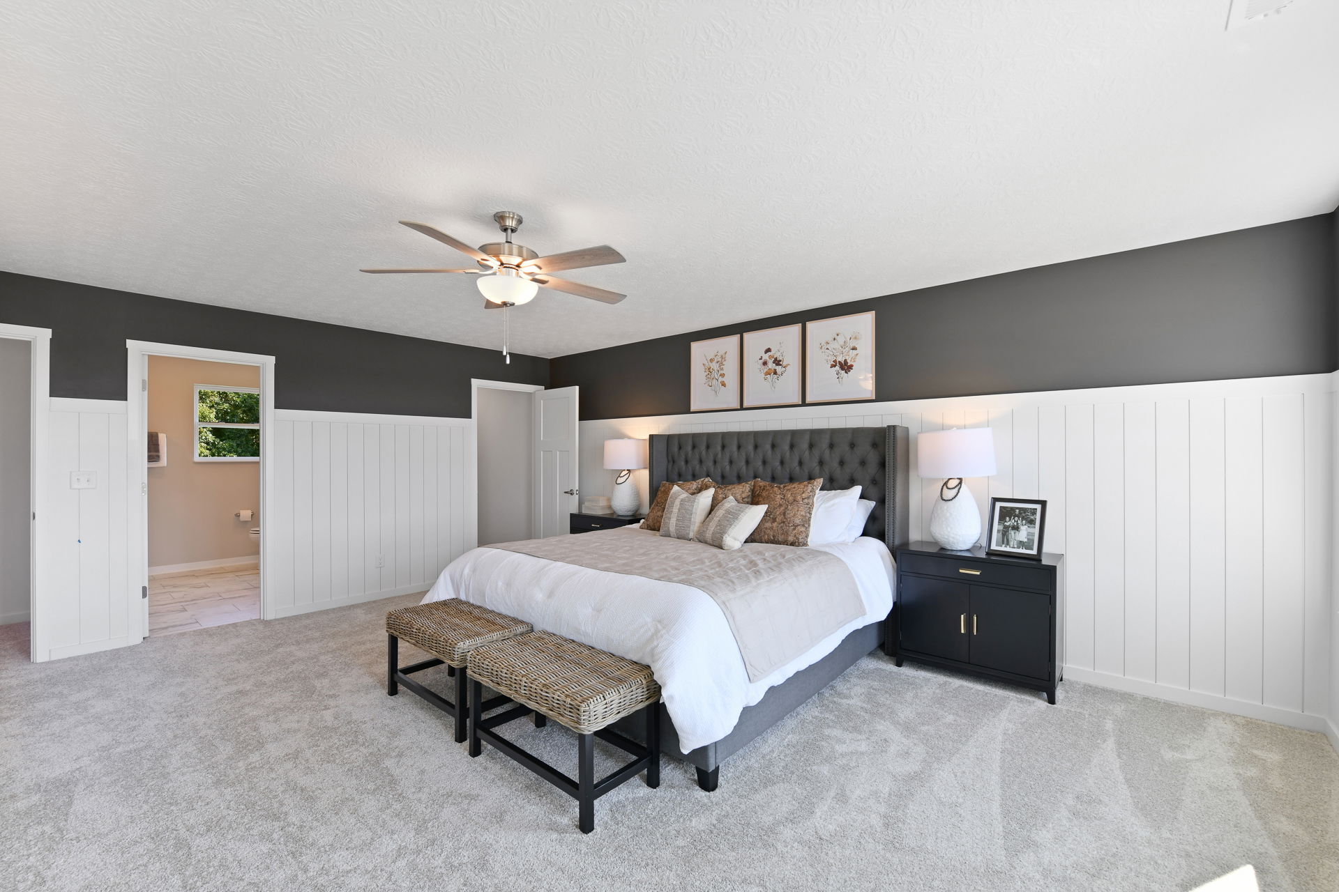 Modern bedroom with a cozy gray-tufted bed, white and black decor, and elegant artwork above, showcasing contemporary interior design.