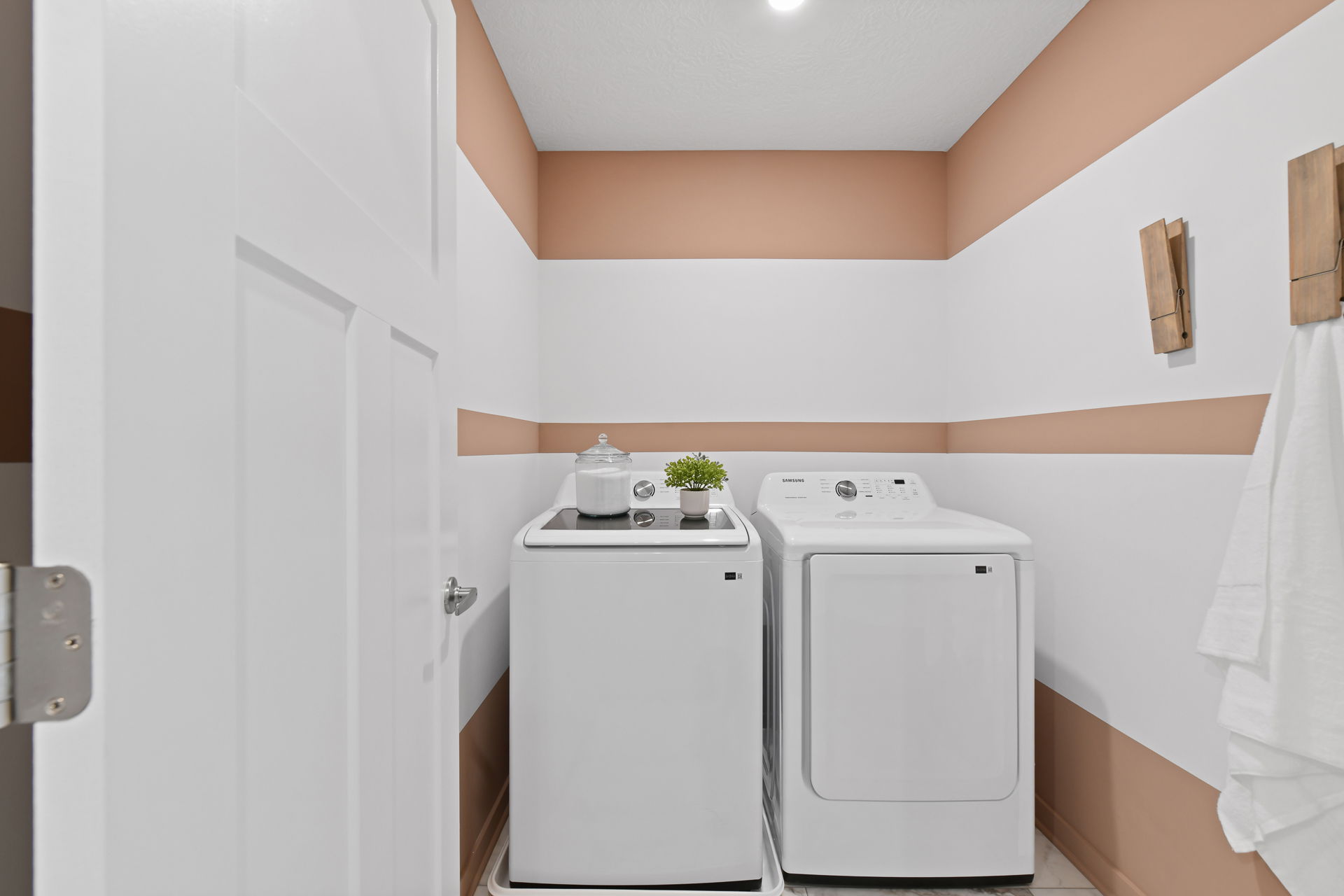 Modern laundry room with a washing machine, dryer, and stylish tan and white striped walls.