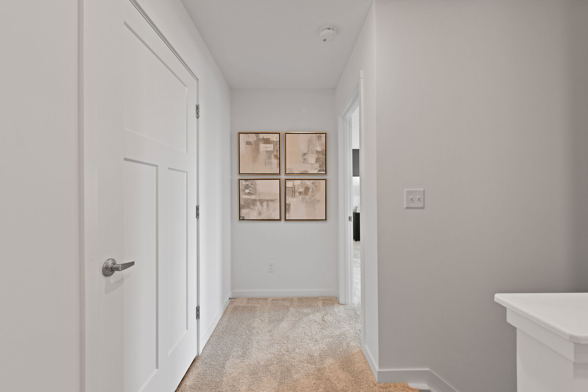 Modern hallway with white walls and four abstract paintings above a carpeted floor.