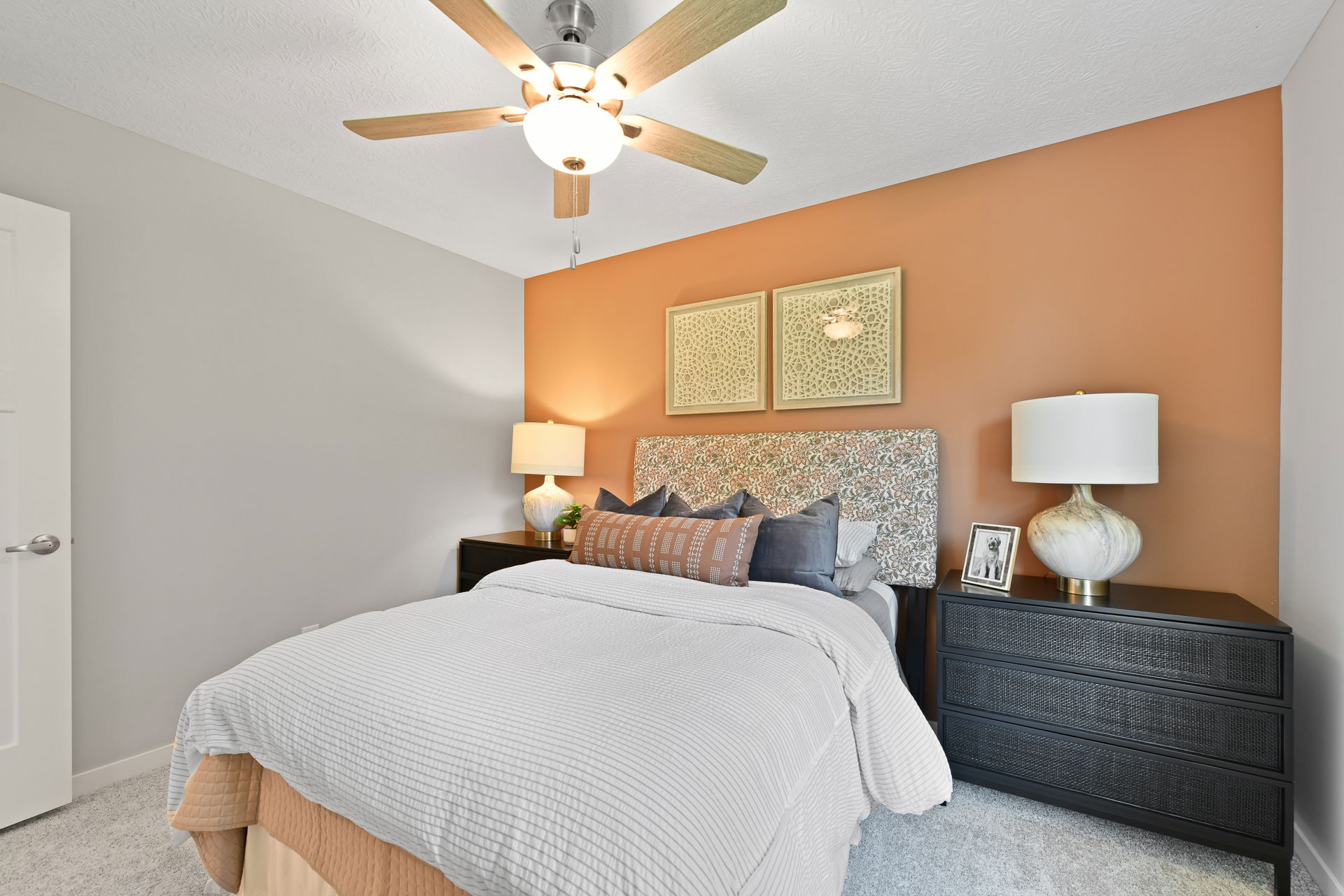 Modern bedroom with stylish decor featuring a patterned headboard, warm orange accent wall, and ceiling fan.