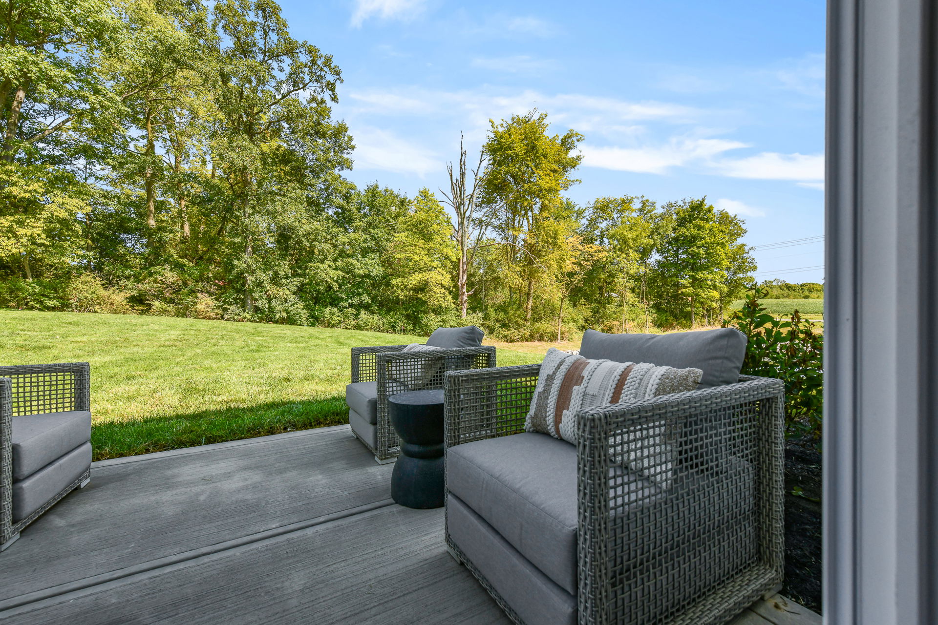 Outdoor patio with wicker furniture overlooking a lush green lawn and trees under a blue sky.