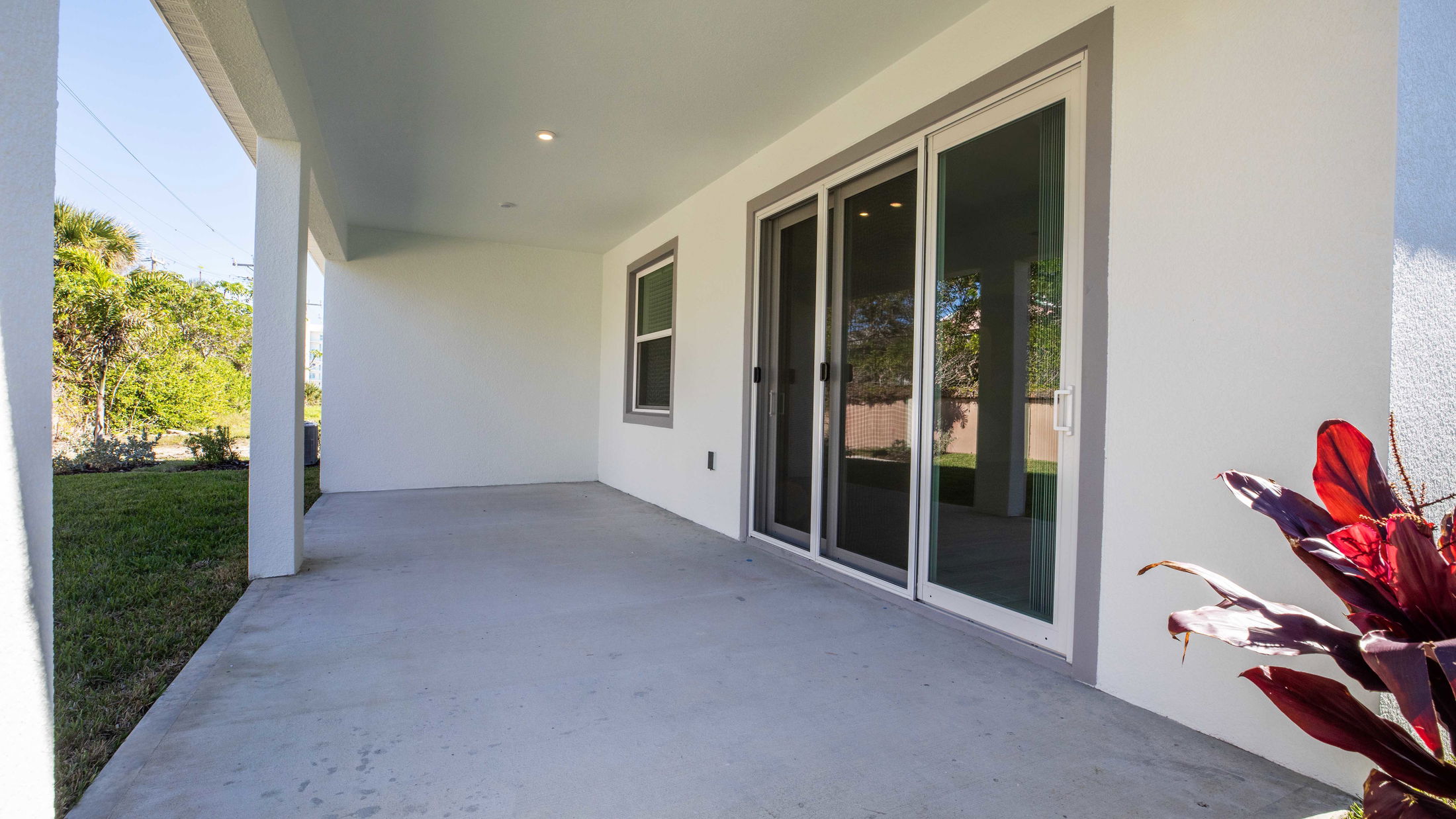 Covered patio with sliding glass doors leading to a grassy backyard surrounded by greenery.