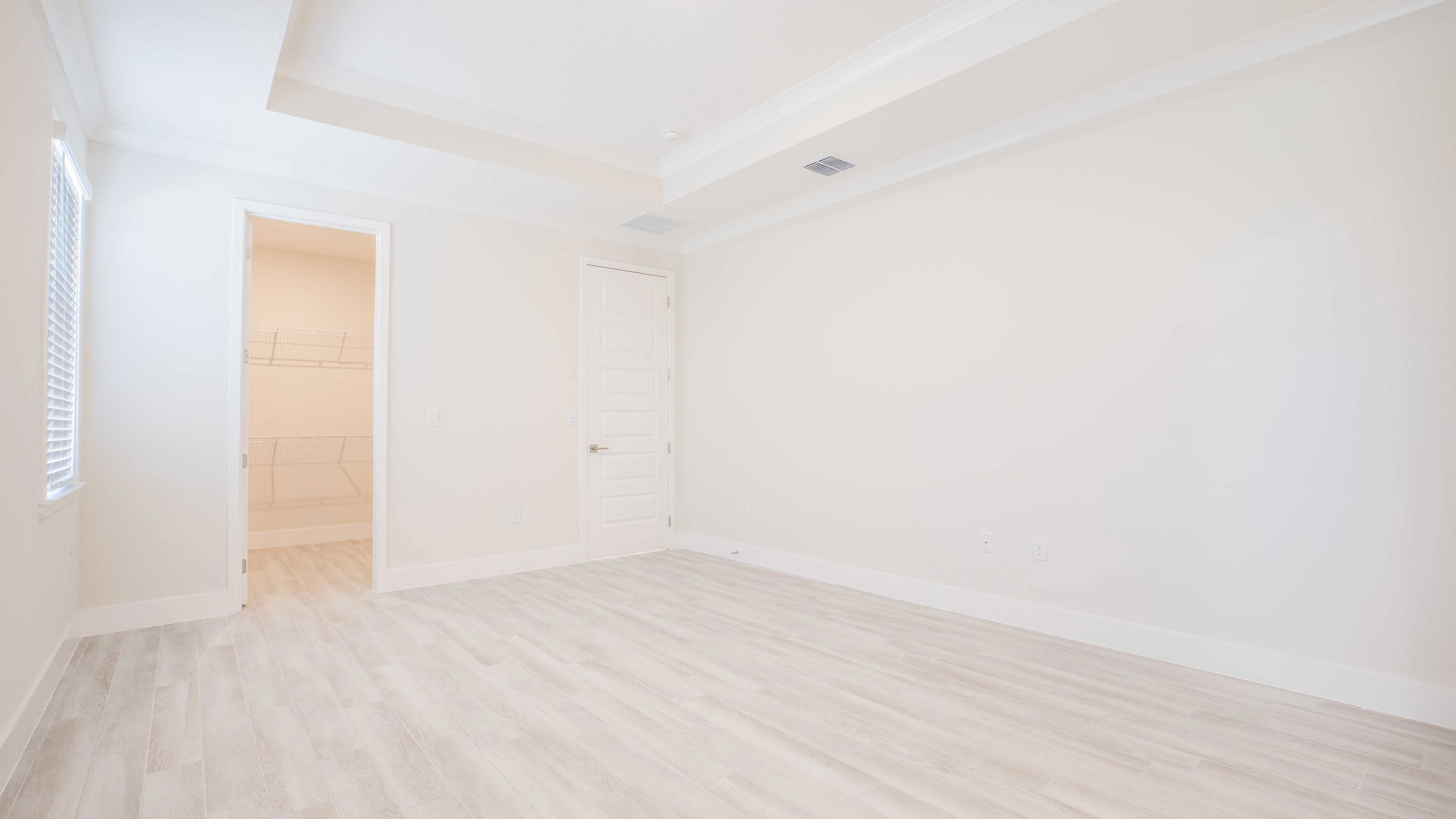 Empty room with light wood flooring, white walls, and an open door leading to a closet with shelving.